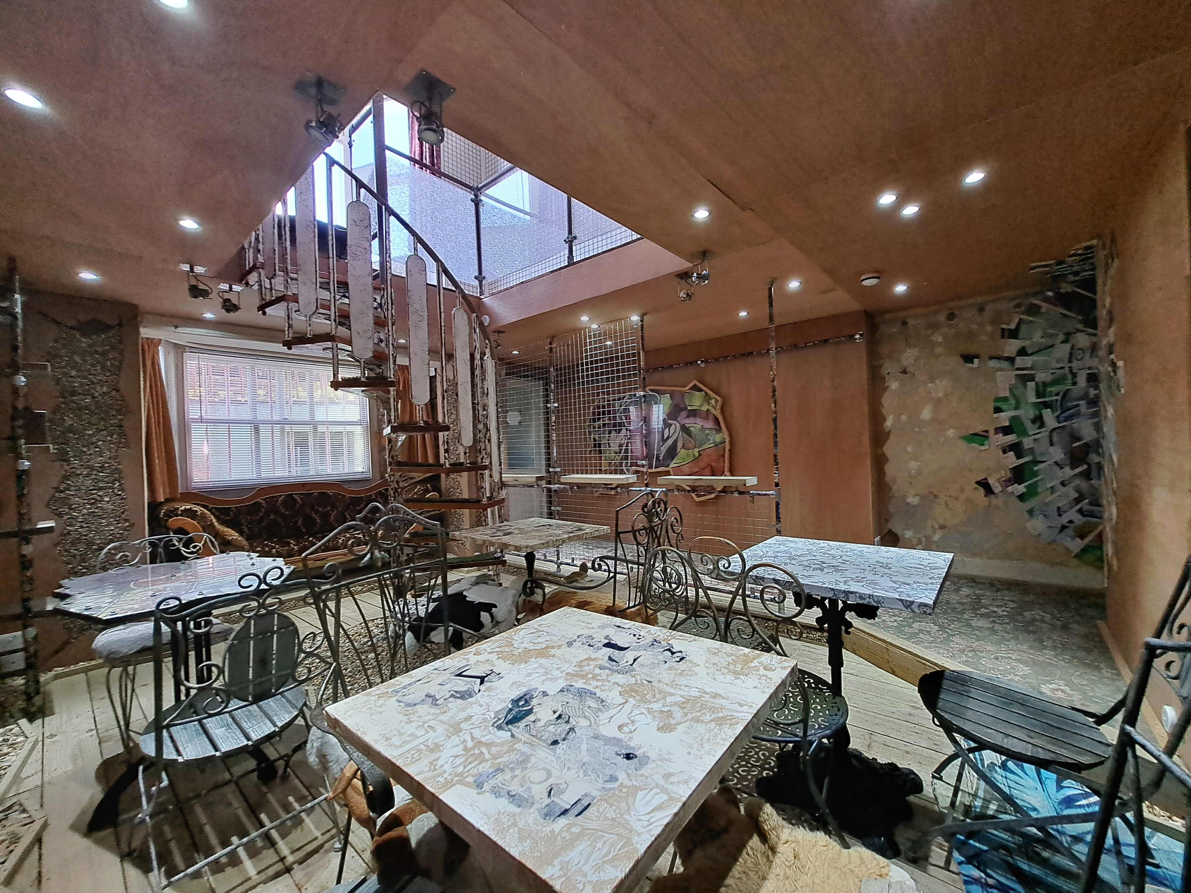 A multi-level room with a spiral staircase, various tables, and walls displaying an eclectic mix of decor and photographs.
