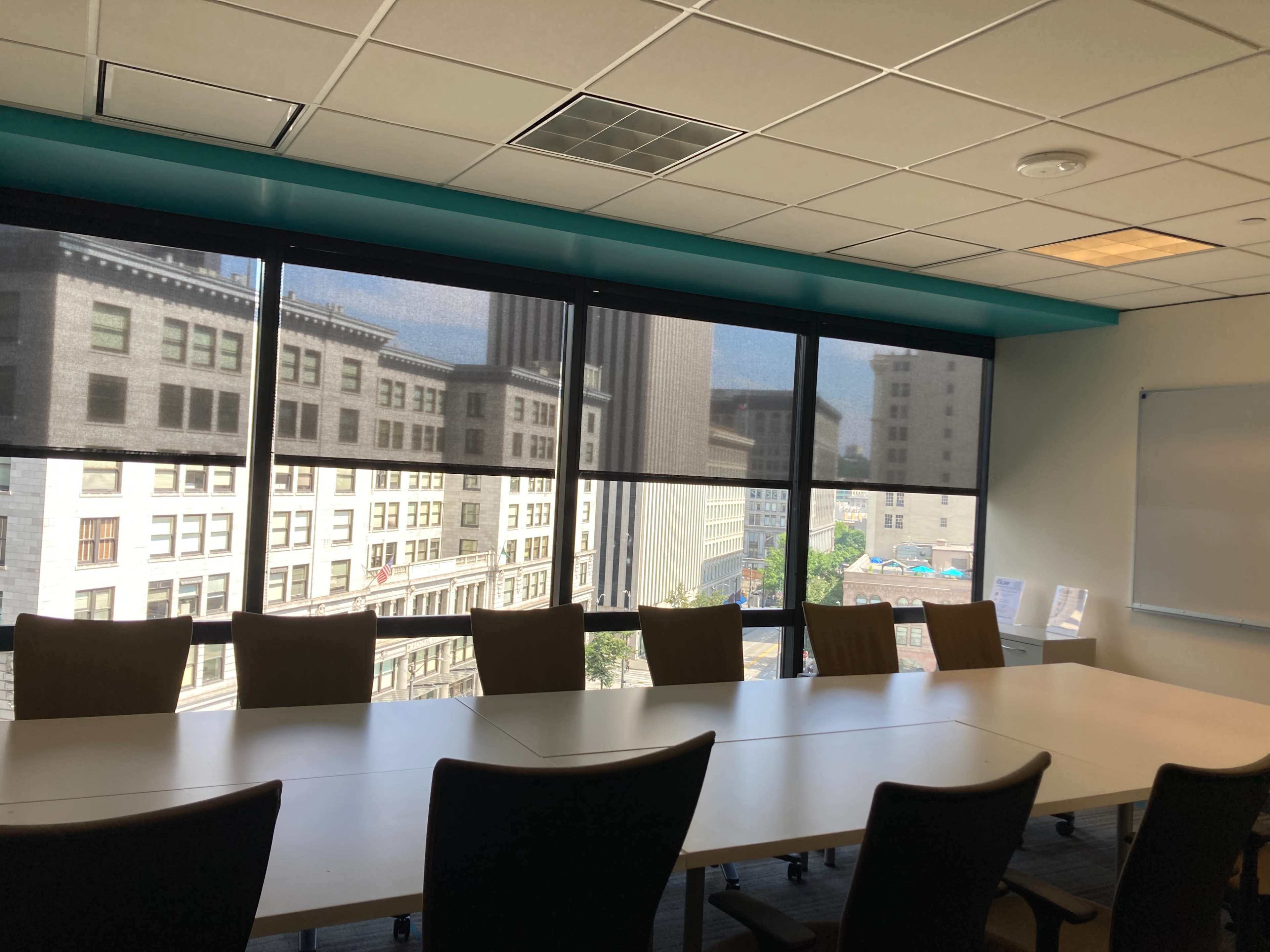 A conference room features a long table surrounded by chairs and large windows overlooking a cityscape.