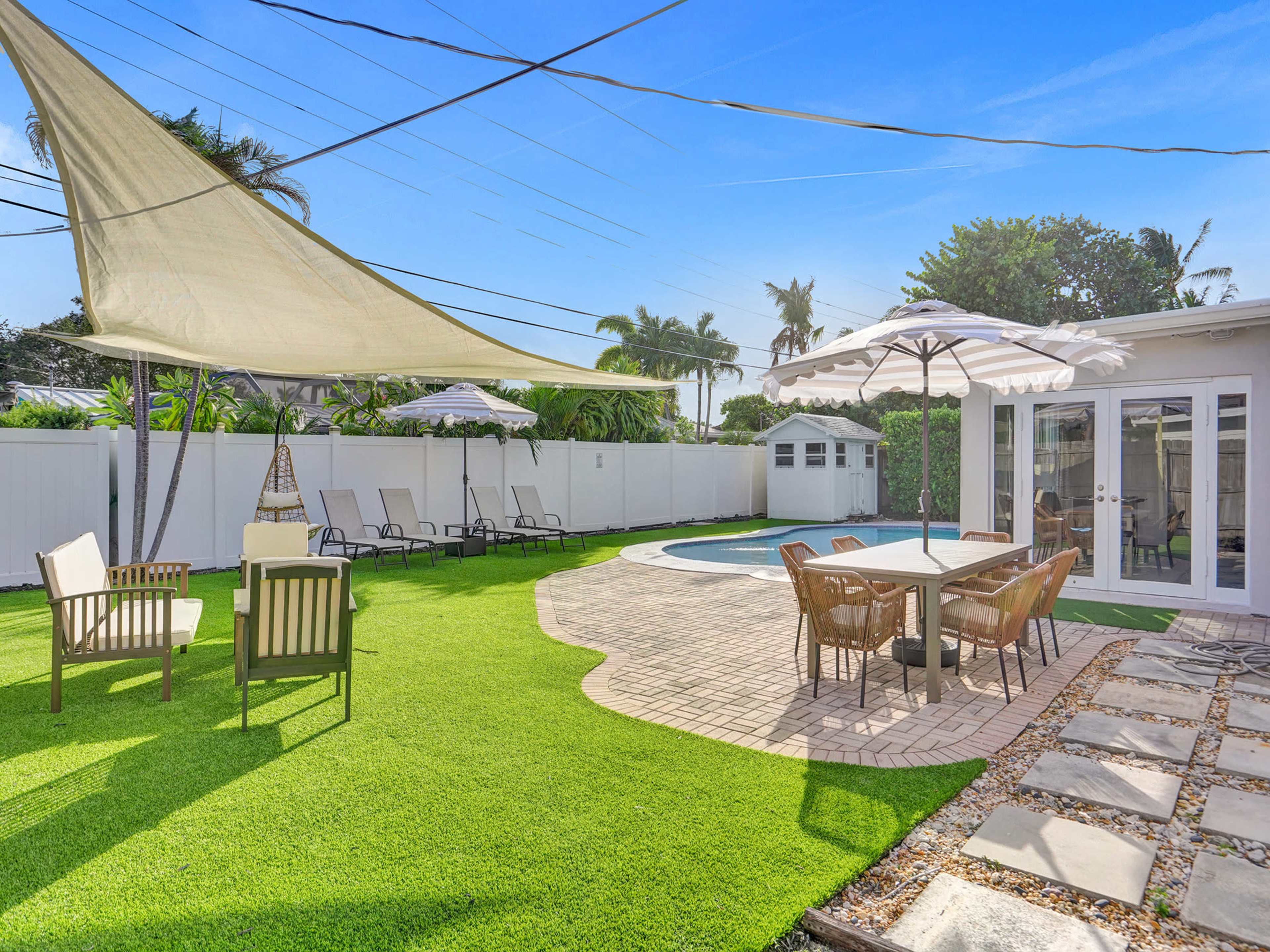An outdoor patio area with a pool surrounded by lounge chairs, tables, and a shaded seating area.