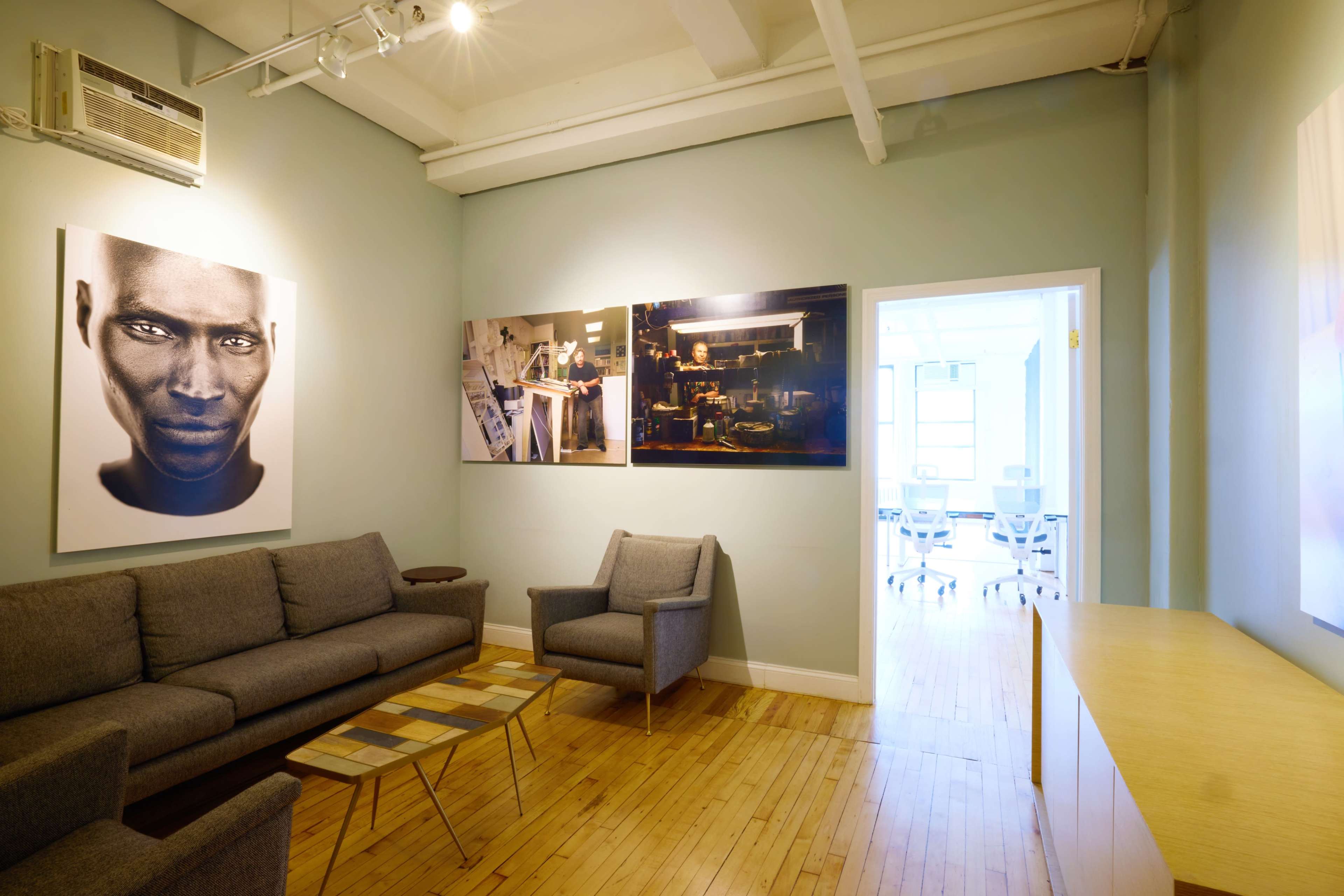 A modern lounge area featuring gray sofas and armchairs, artwork on the walls, and a wooden coffee table in a spacious room with wooden flooring.