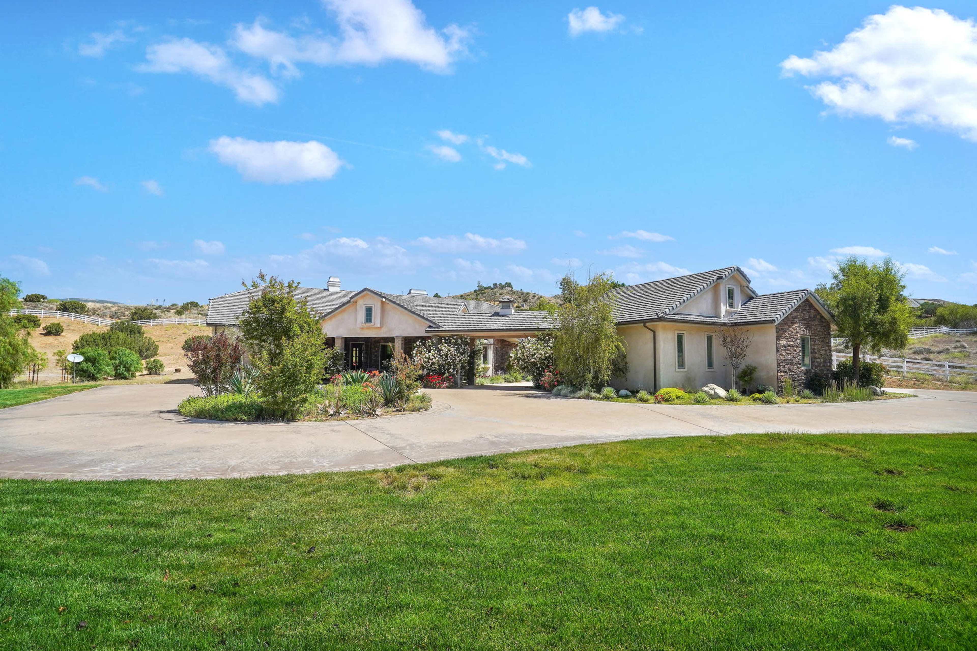 A single-story house with a stone accent and a landscaped front yard is set against a blue sky with scattered clouds.