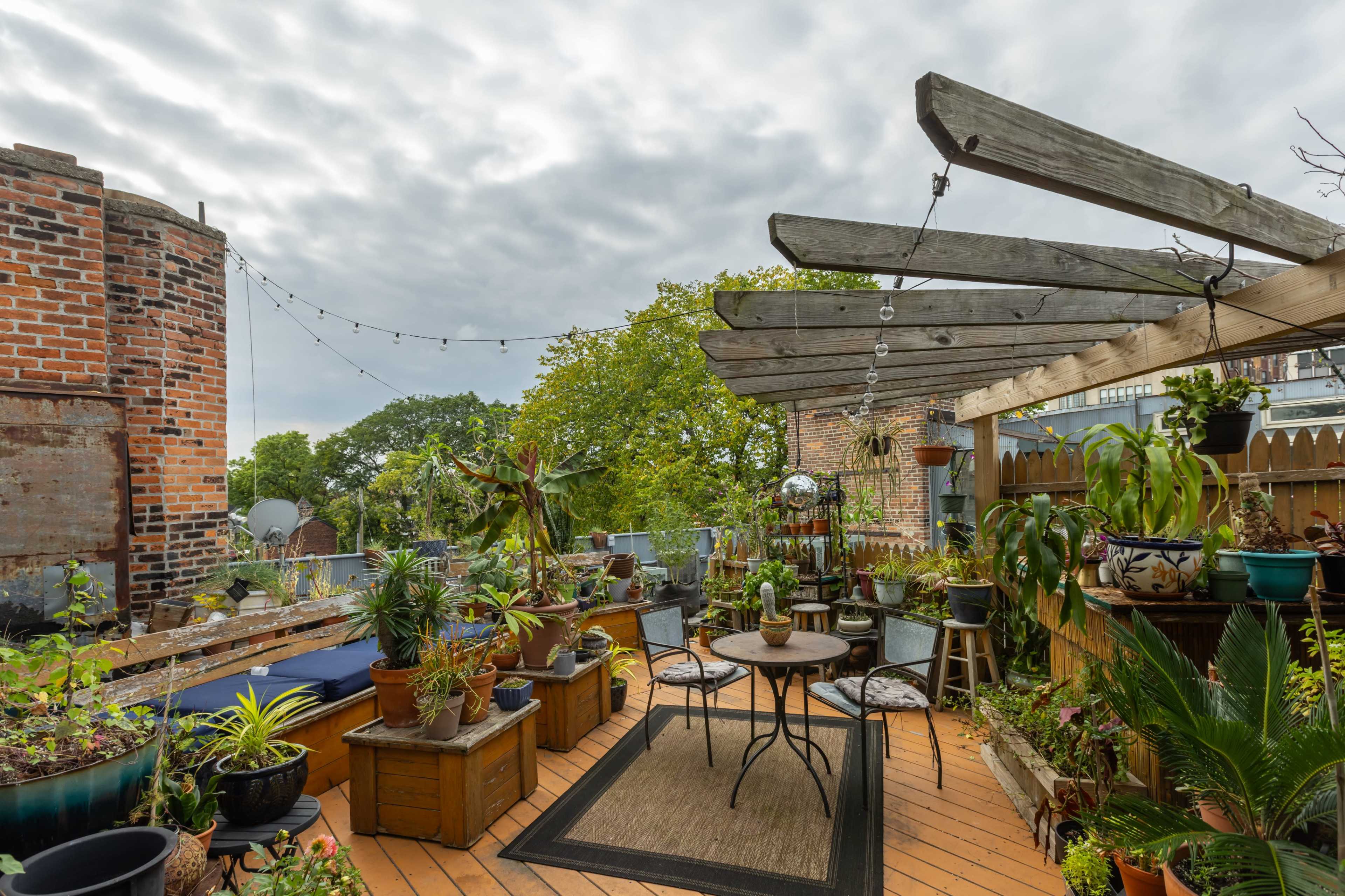 The rooftop terrace features a wooden pergola and is filled with various potted plants, seating arrangements, and decorative elements.