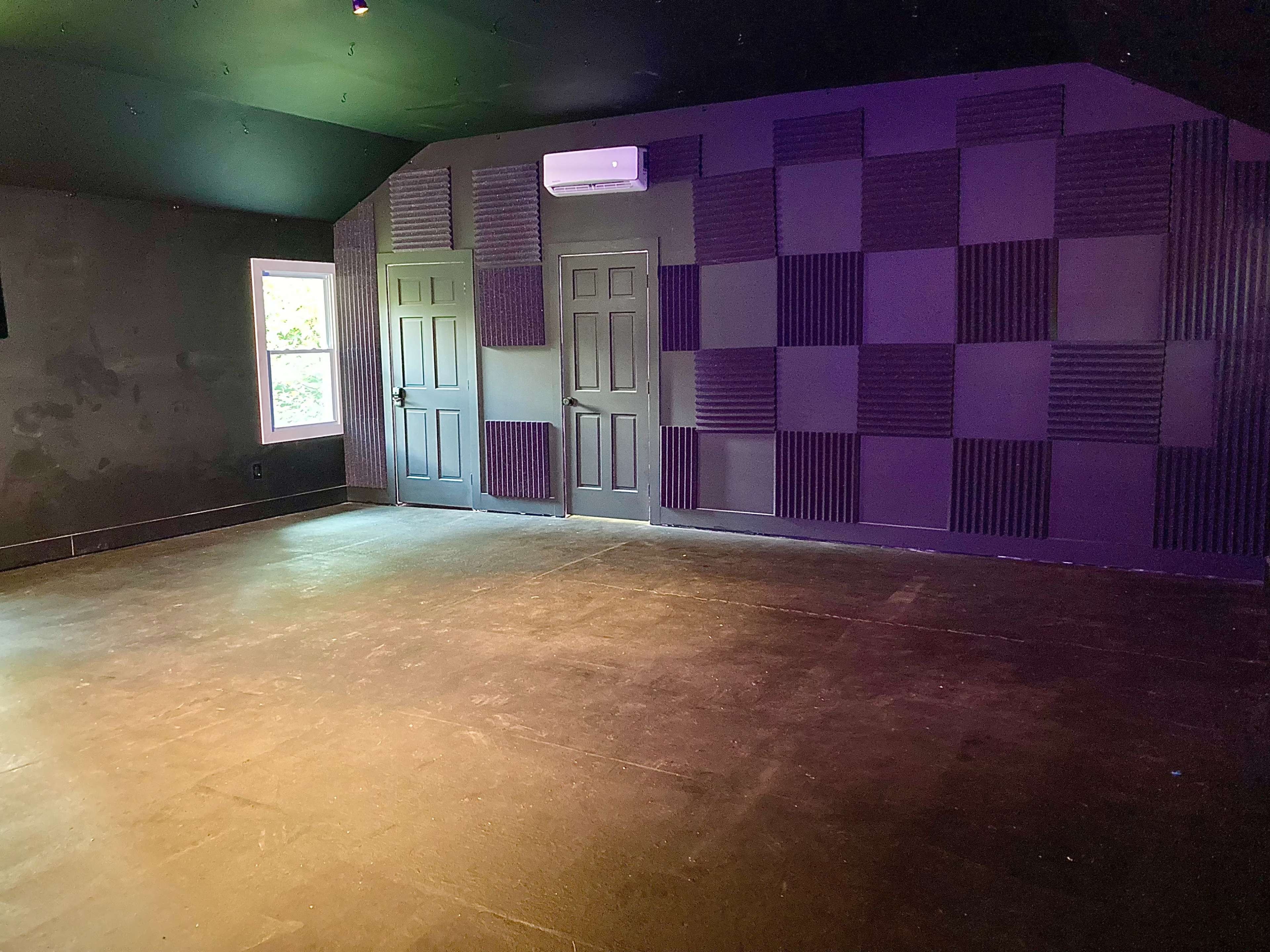 An empty room with two closed doors and soundproofing panels on the walls, illuminated by natural light from a window.