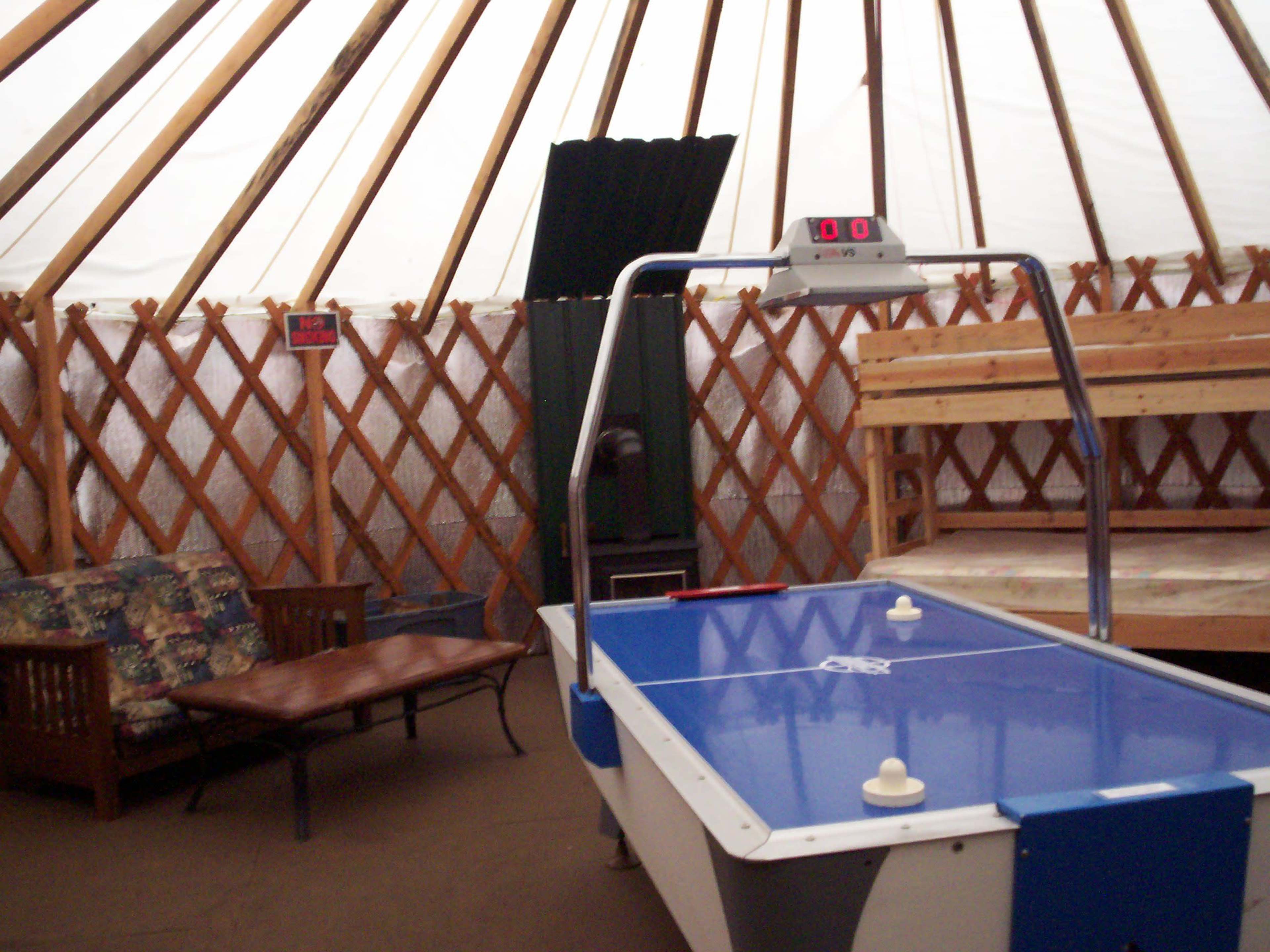 The interior of a yurt features an air hockey table, a couch, and a wooden bunk bed.