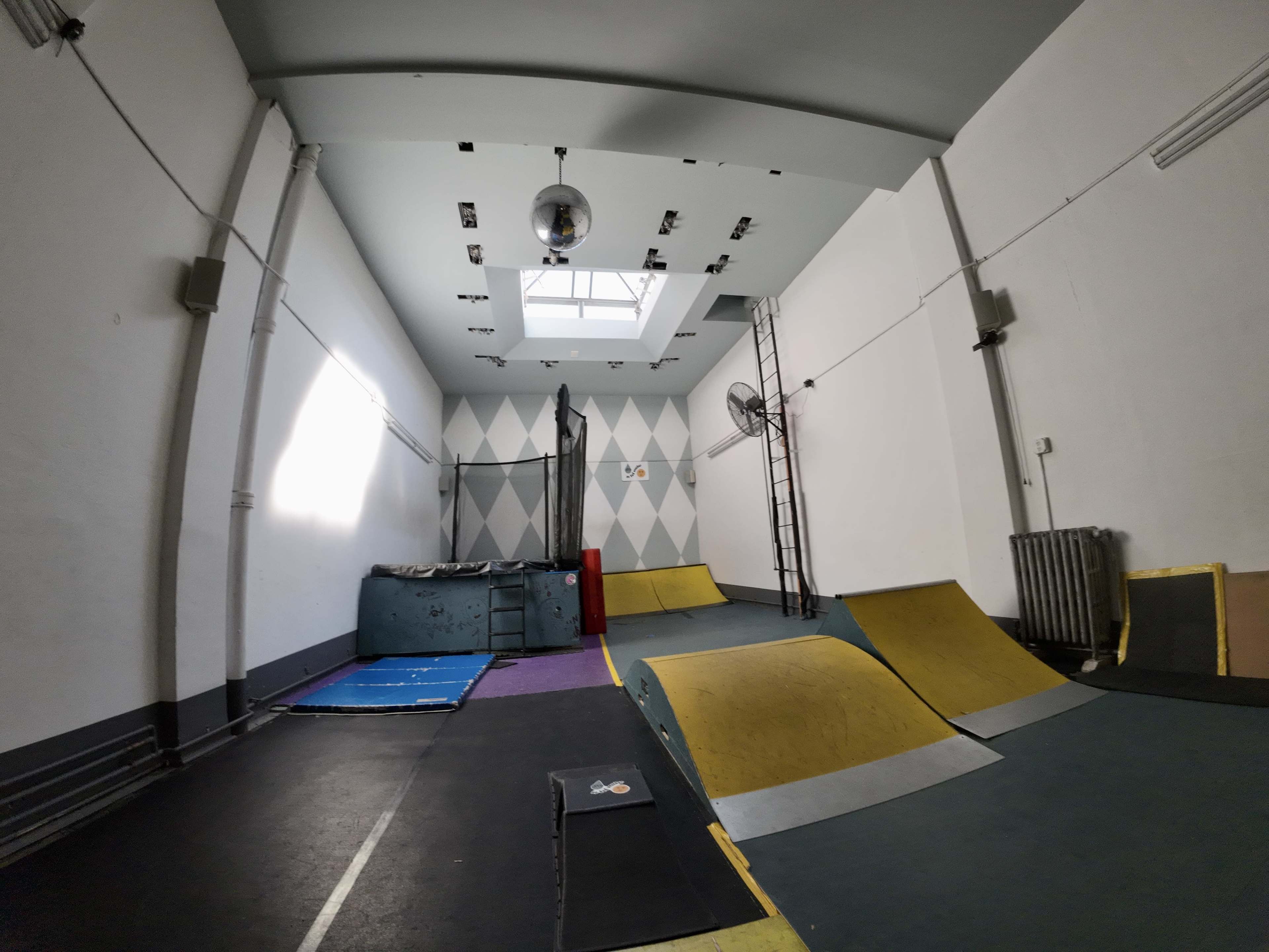 The image shows an indoor skatepark with ramps, a padded area, and a skylight in the ceiling.