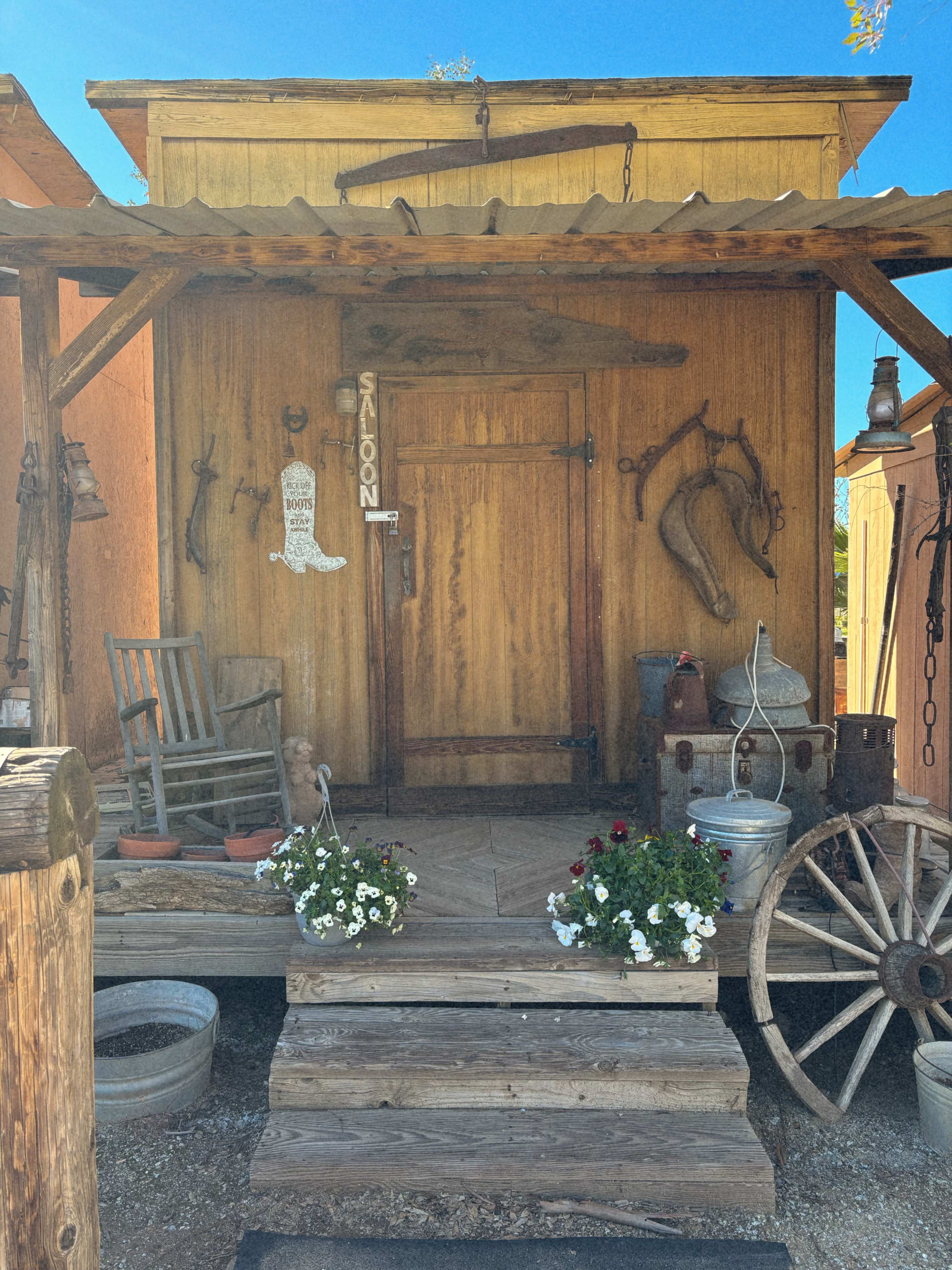 A wooden saloon front with a rocking chair, decorative horseshoes, and flower pots on the porch steps.
