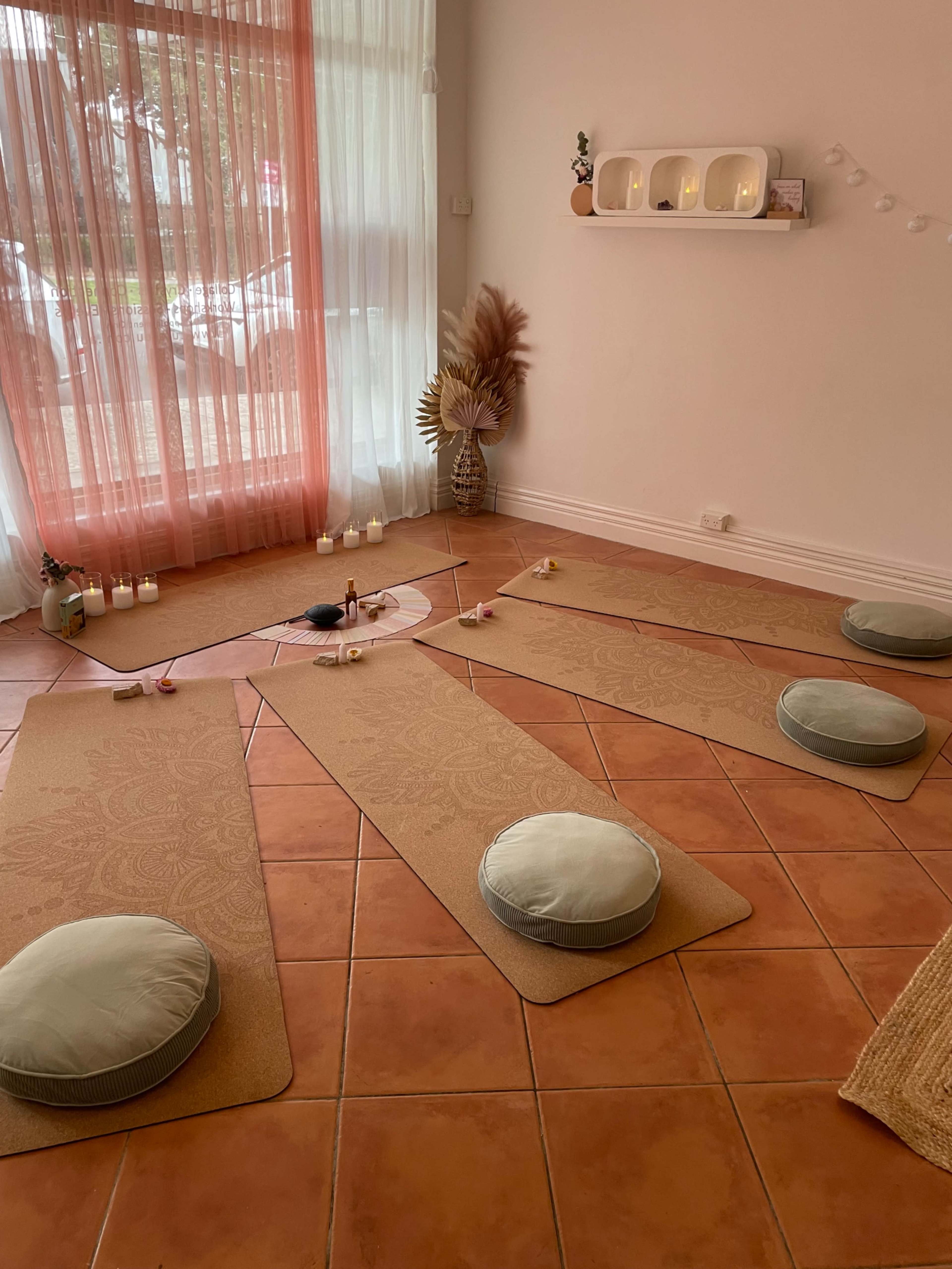 The image shows a serene meditation space with yoga mats arranged on a tiled floor, surrounded by candles and decorative elements.