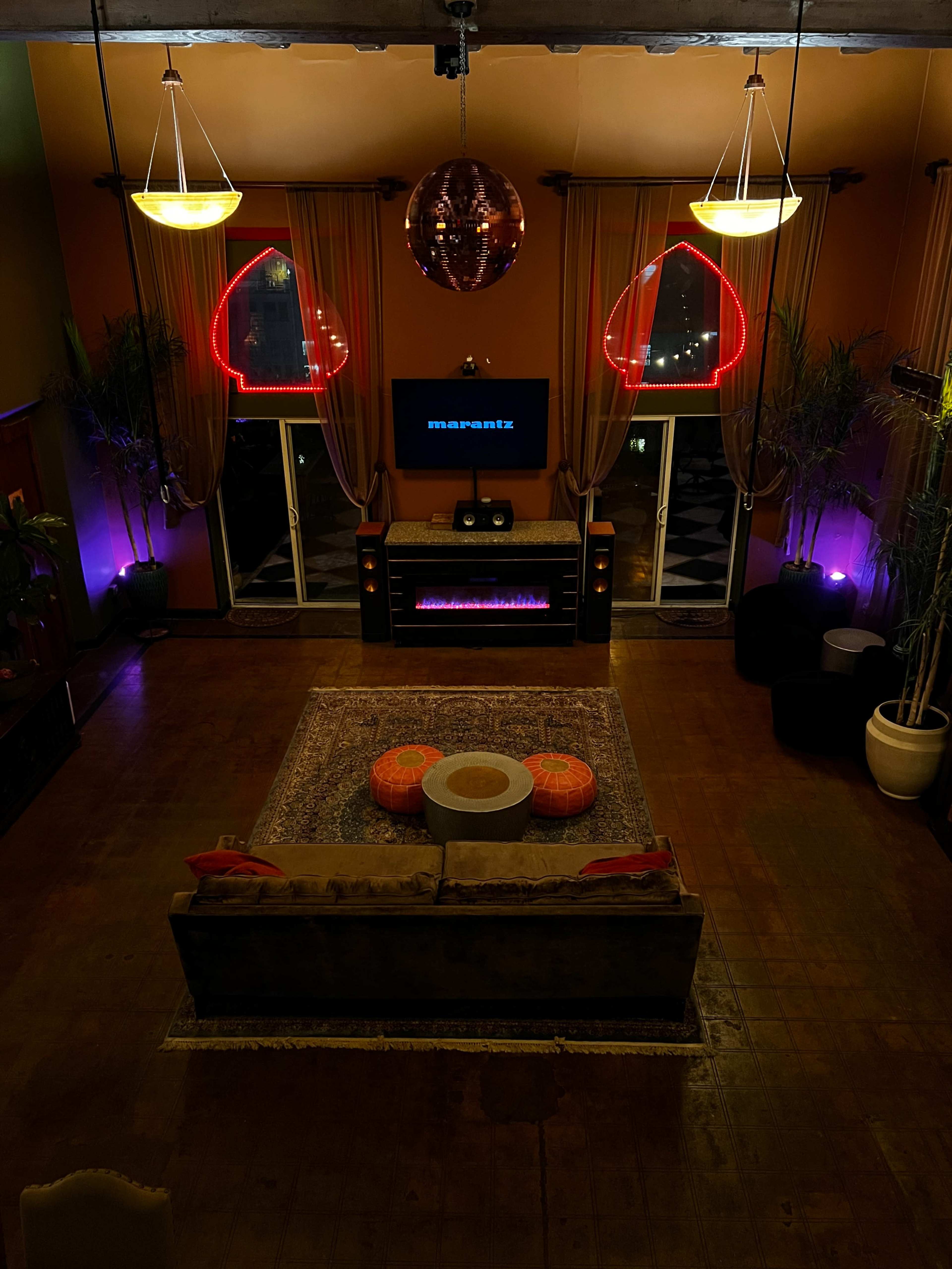 A spacious interior with a large, circular coffee table, a central sofa, and colorful cushions, illuminated by neon lights and soft overhead fixtures.