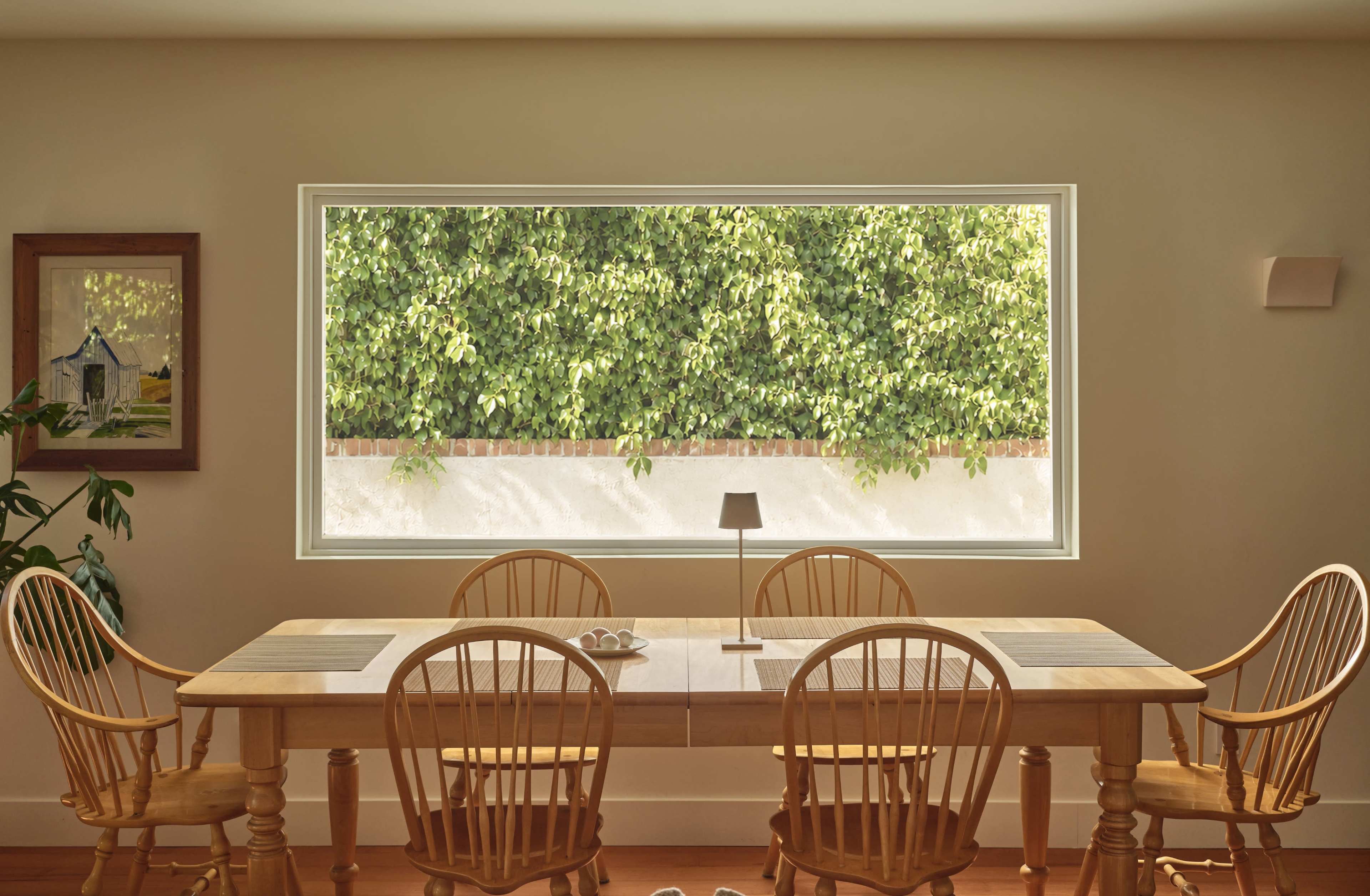 A spacious dining area features a wooden table surrounded by six chairs, with a large window showcasing a view of lush greenery outside.