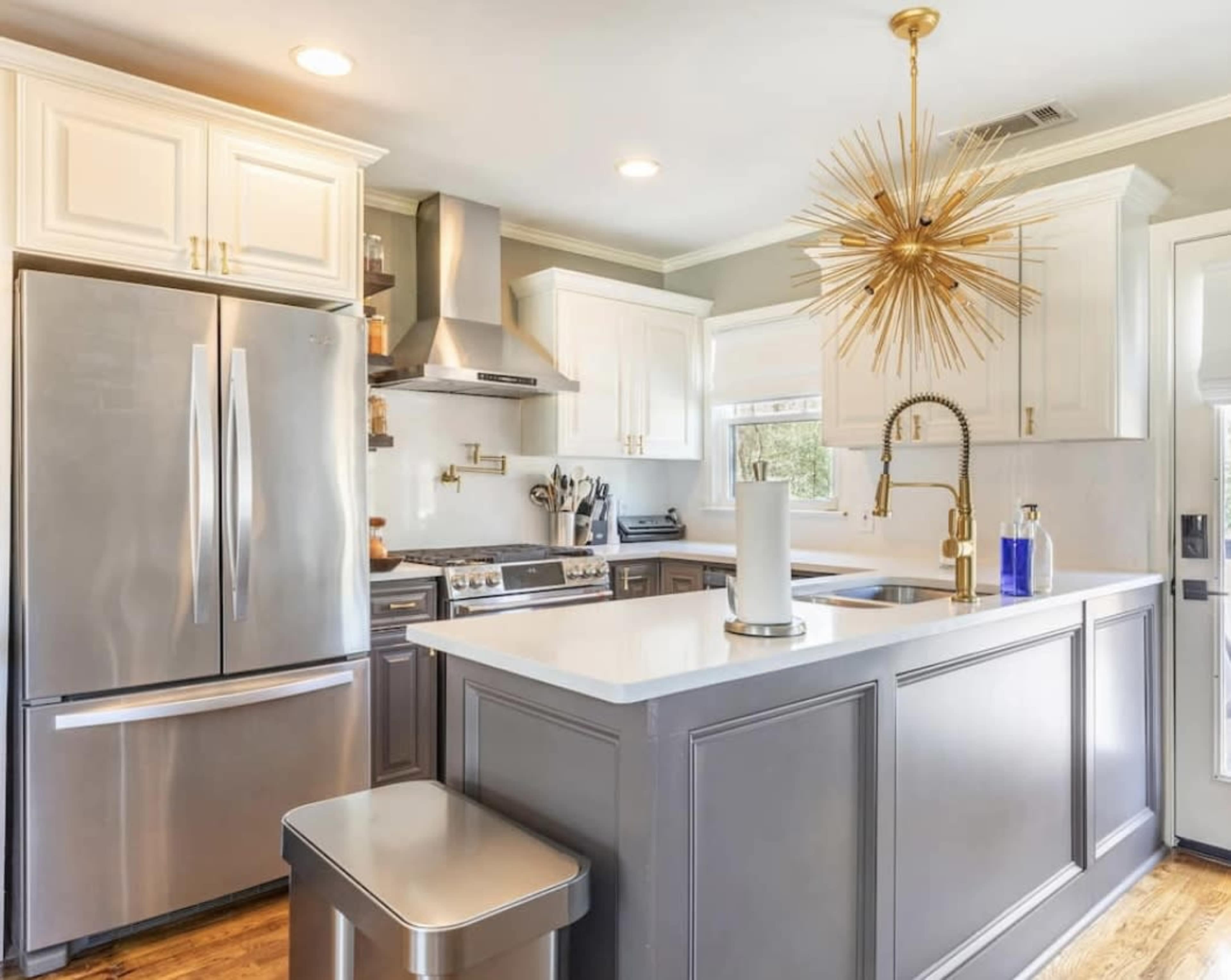 The kitchen features stainless steel appliances, white cabinetry, and a central island with a gold chandelier overhead.