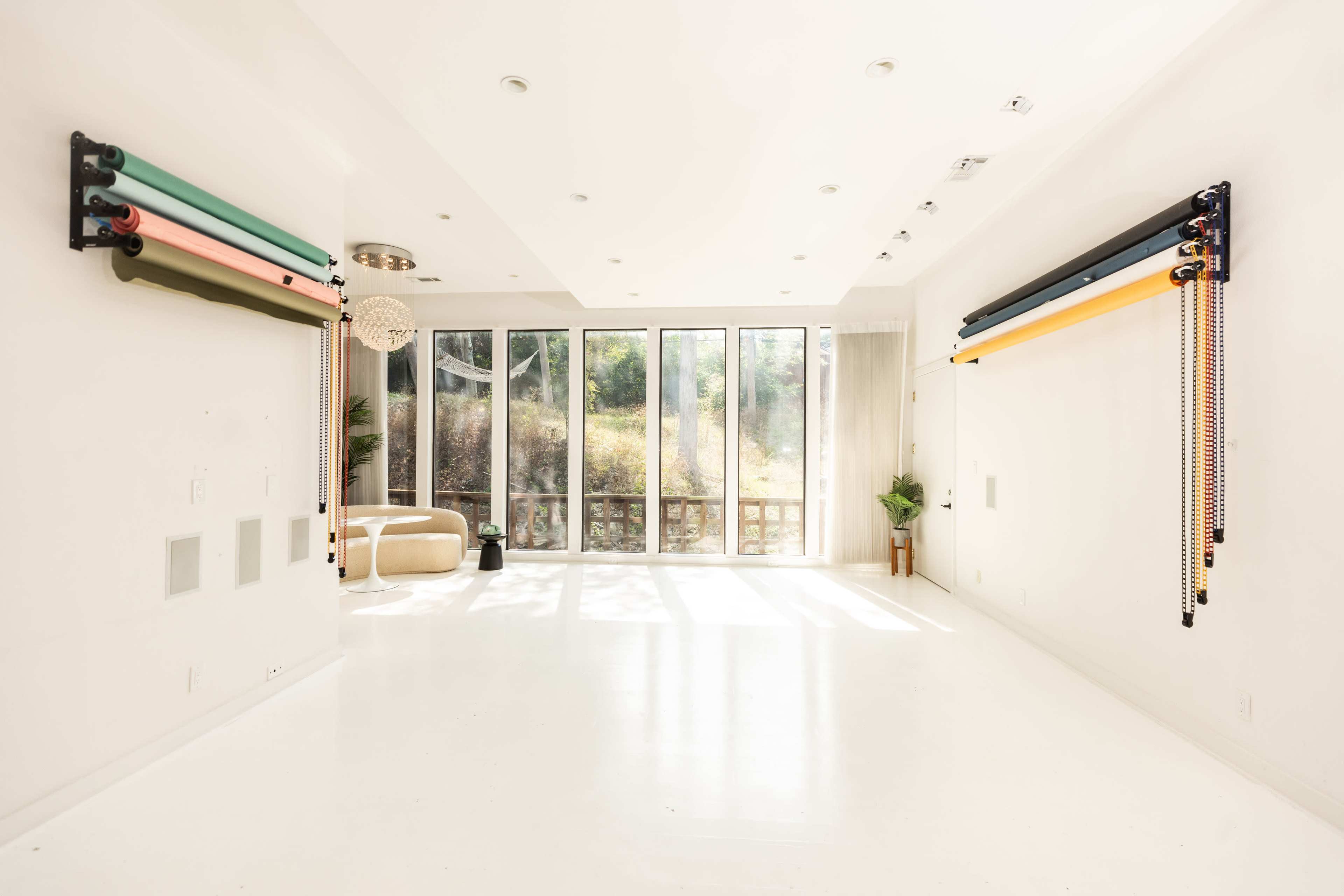 A bright, minimalist room with large windows, featuring colorful resistance bands mounted on the walls and a simple seating area.