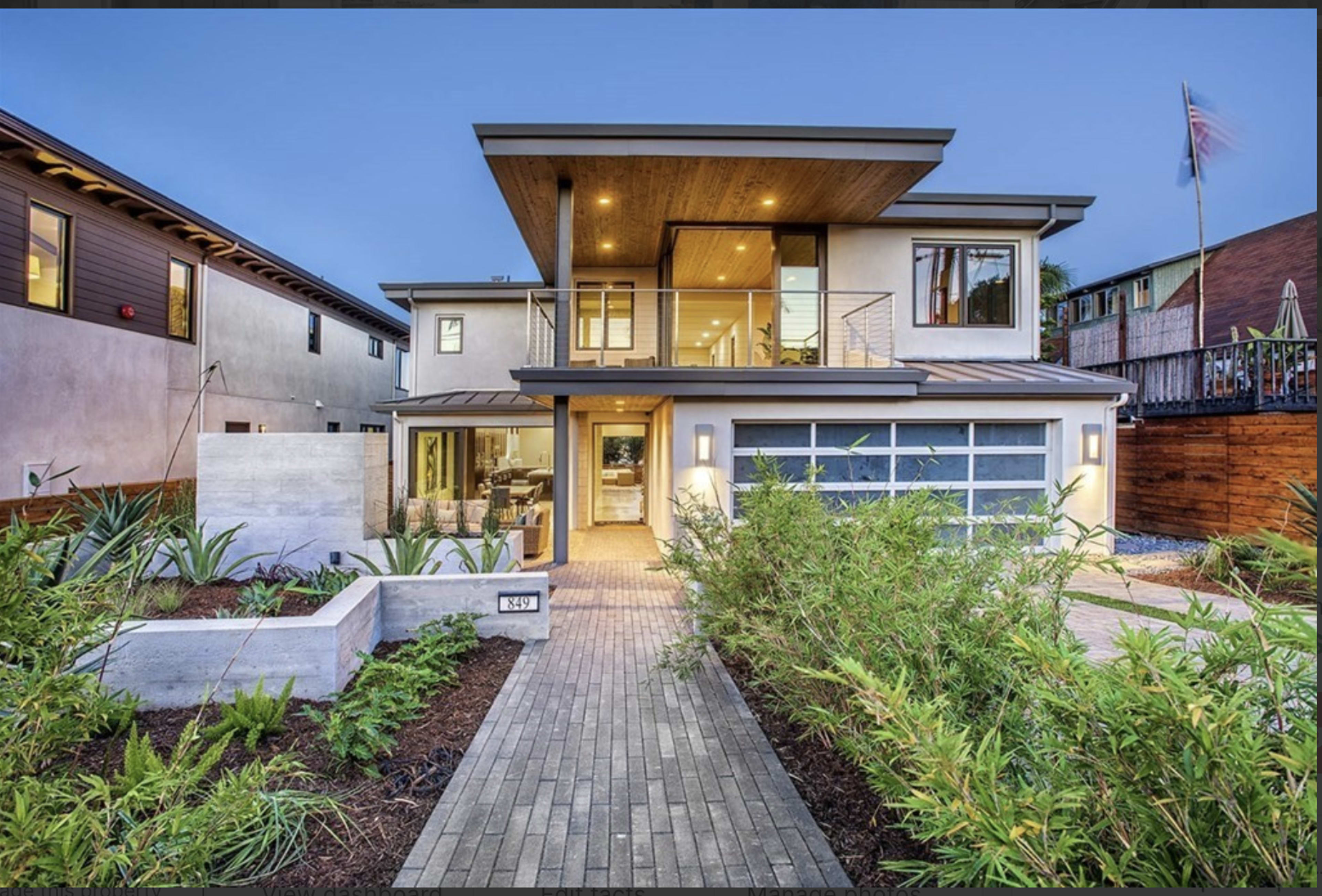 The image shows a modern two-story house with a large front yard, a driveway leading to a garage, and ample landscaping.