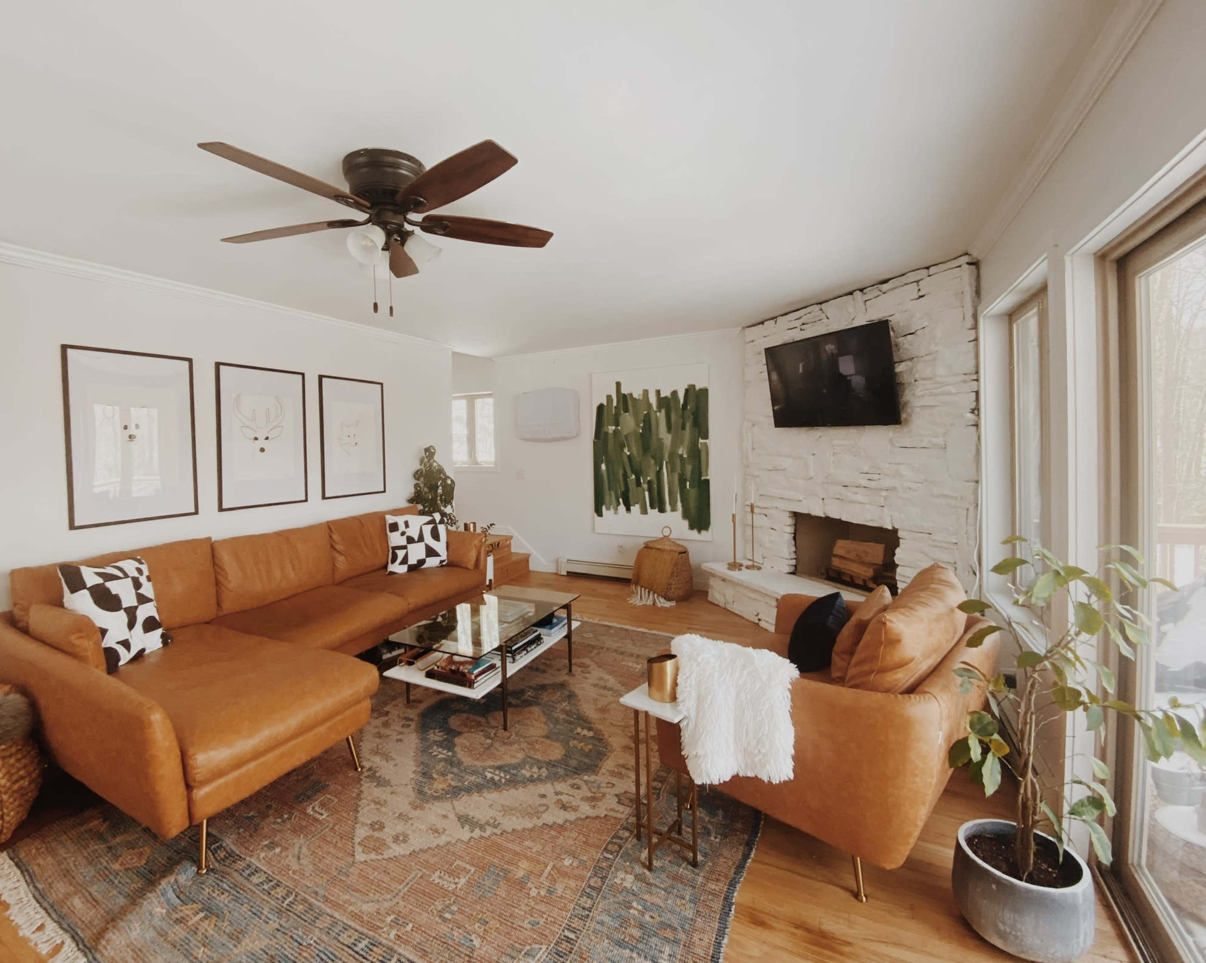 A spacious living room features a large brown sectional sofa, a coffee table, and a stone fireplace, complemented by wall art and large windows.
