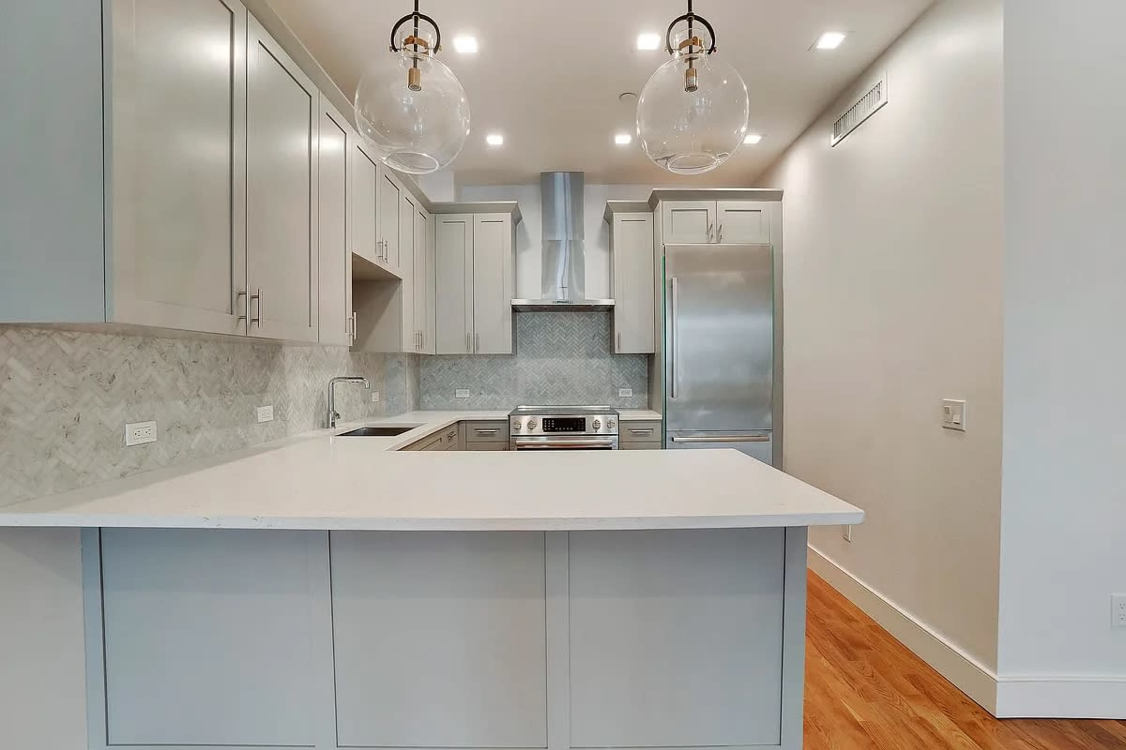 A modern kitchen features light gray cabinetry, a white countertop, and stainless steel appliances.