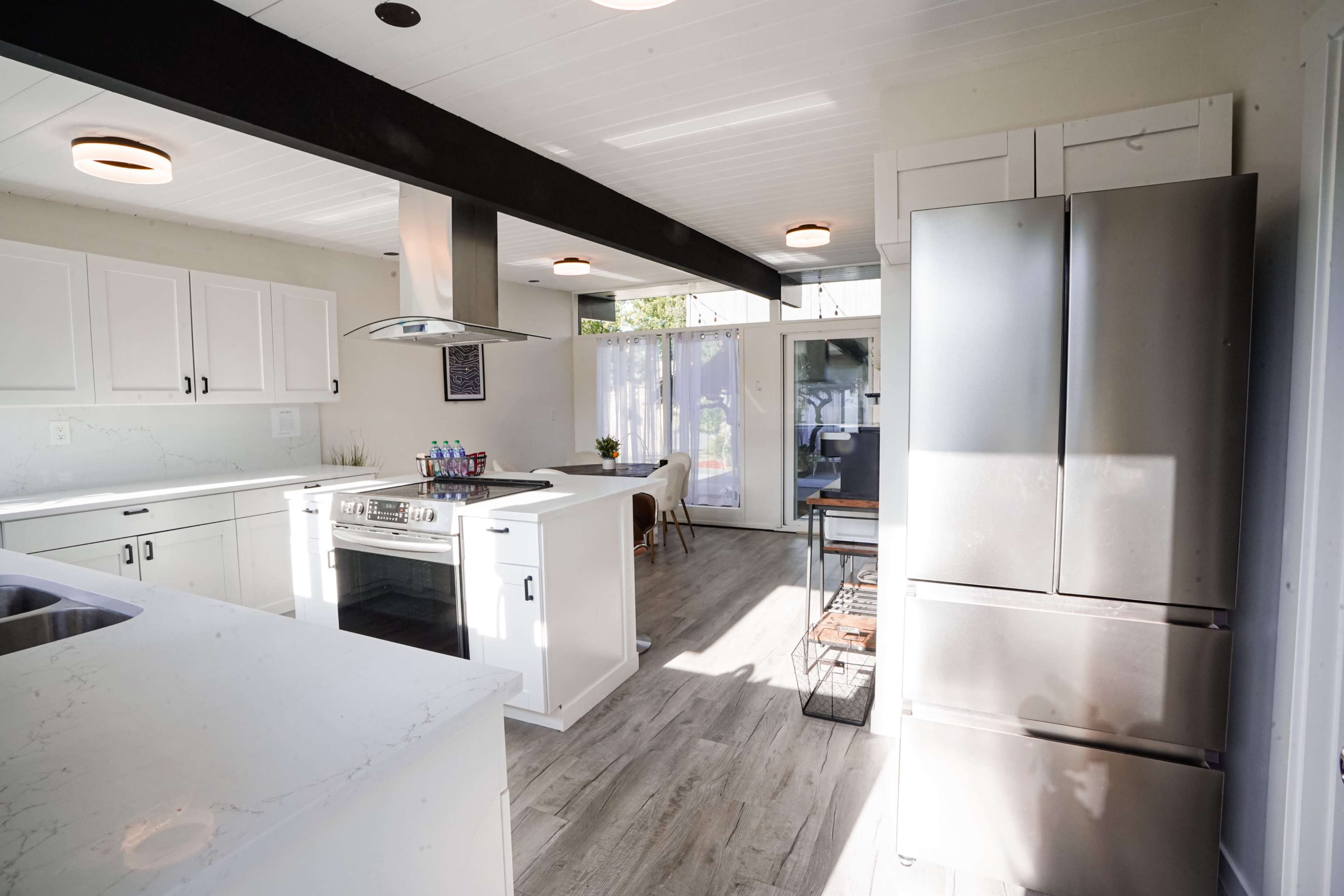 A modern kitchen with white cabinets, a central island with a stove, and stainless steel appliances, including a refrigerator.