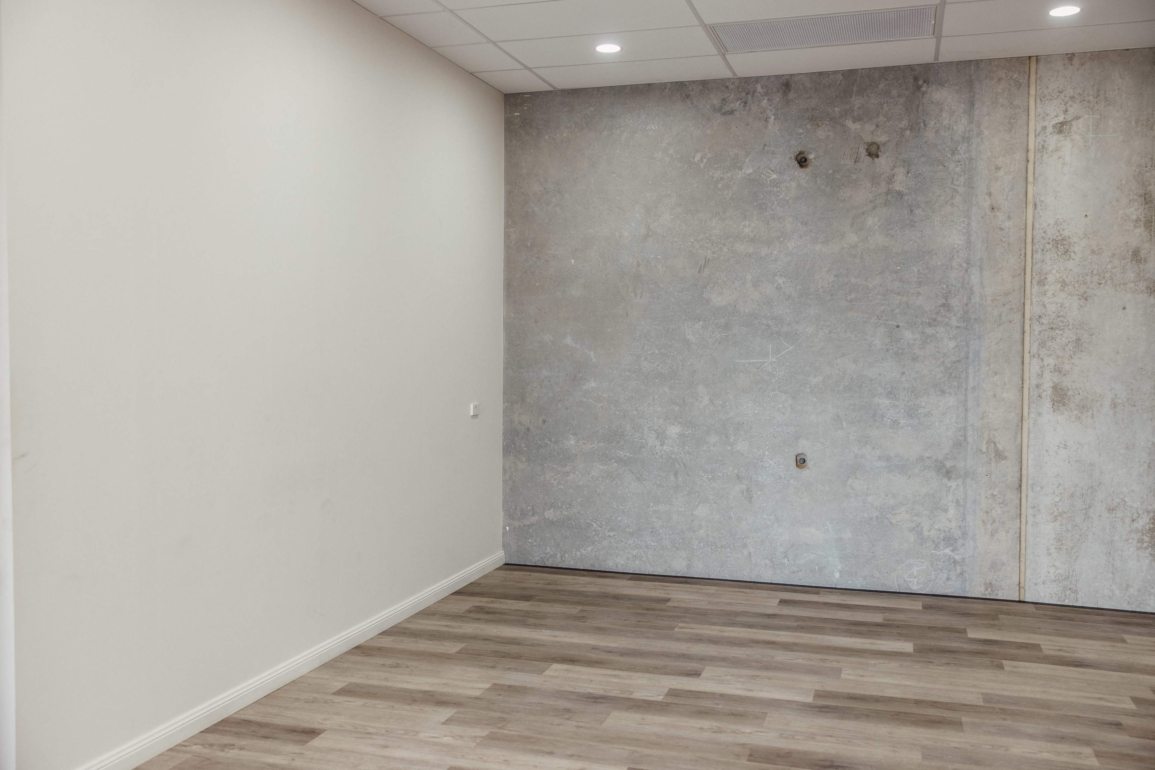 An empty room with one wall featuring a concrete finish and light-colored wooden flooring.