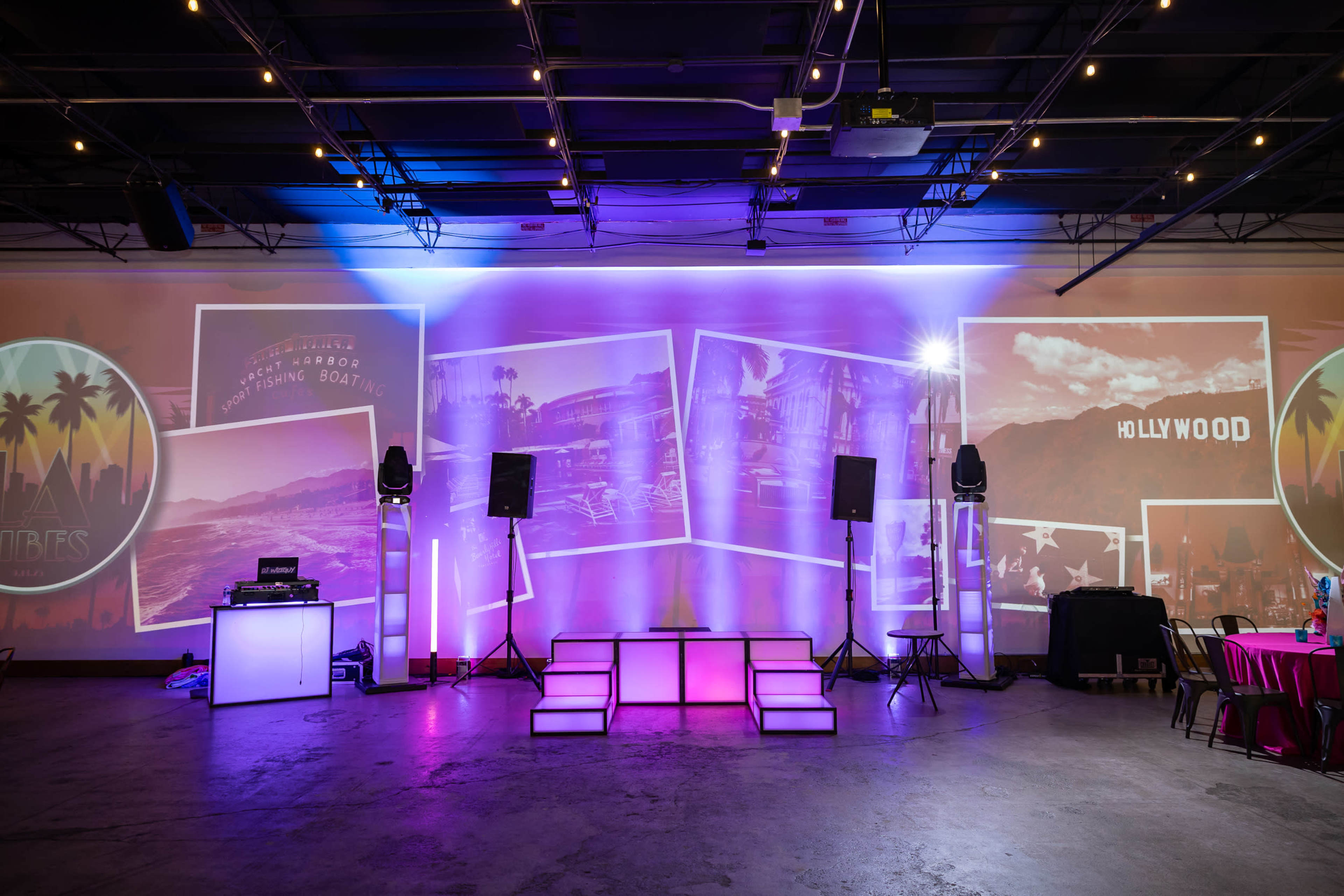 The image shows a party venue with a DJ setup, illuminated by colorful lights and large projected images on a wall.
