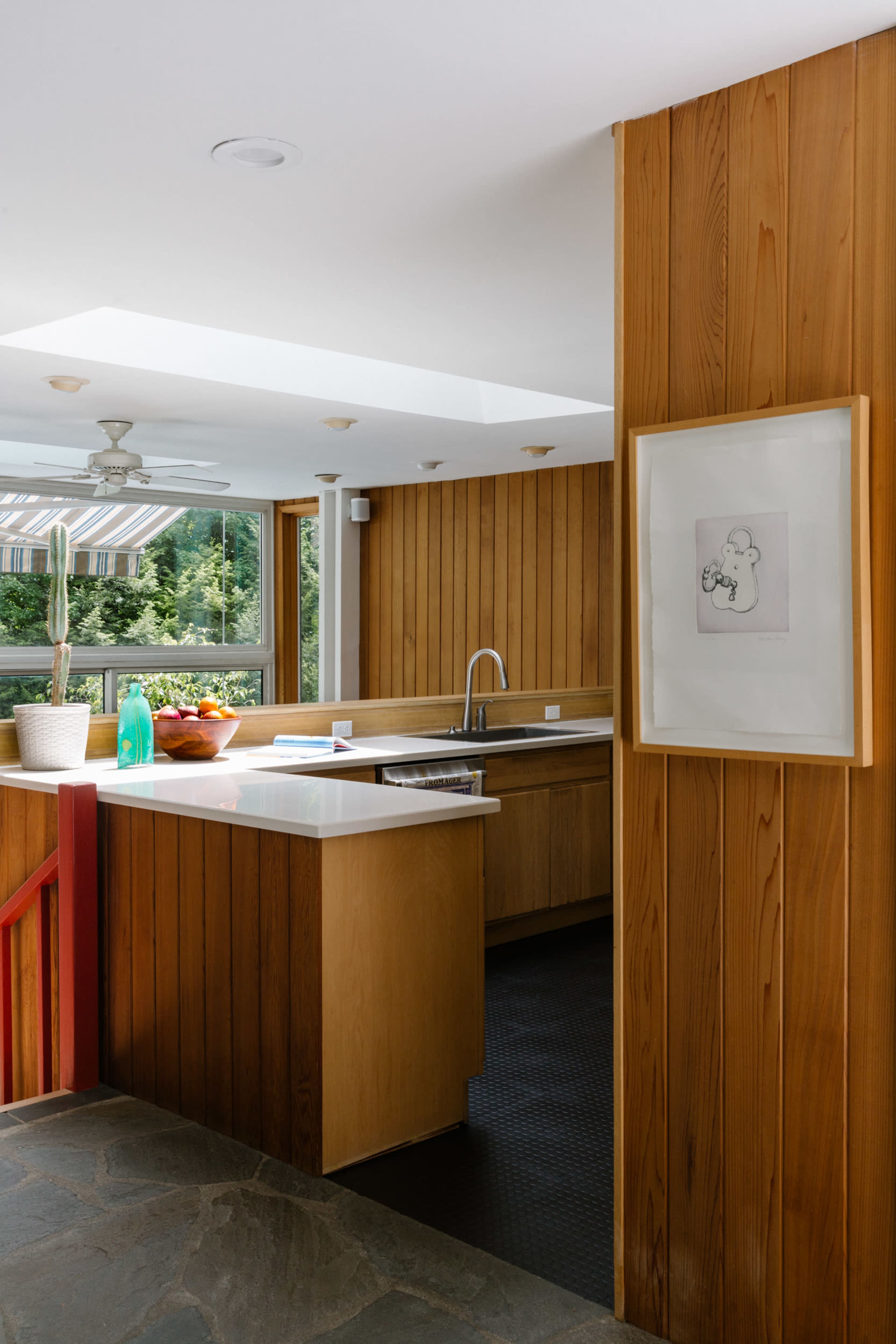A modern kitchen with wooden paneling, a central island, and a large window letting in natural light.