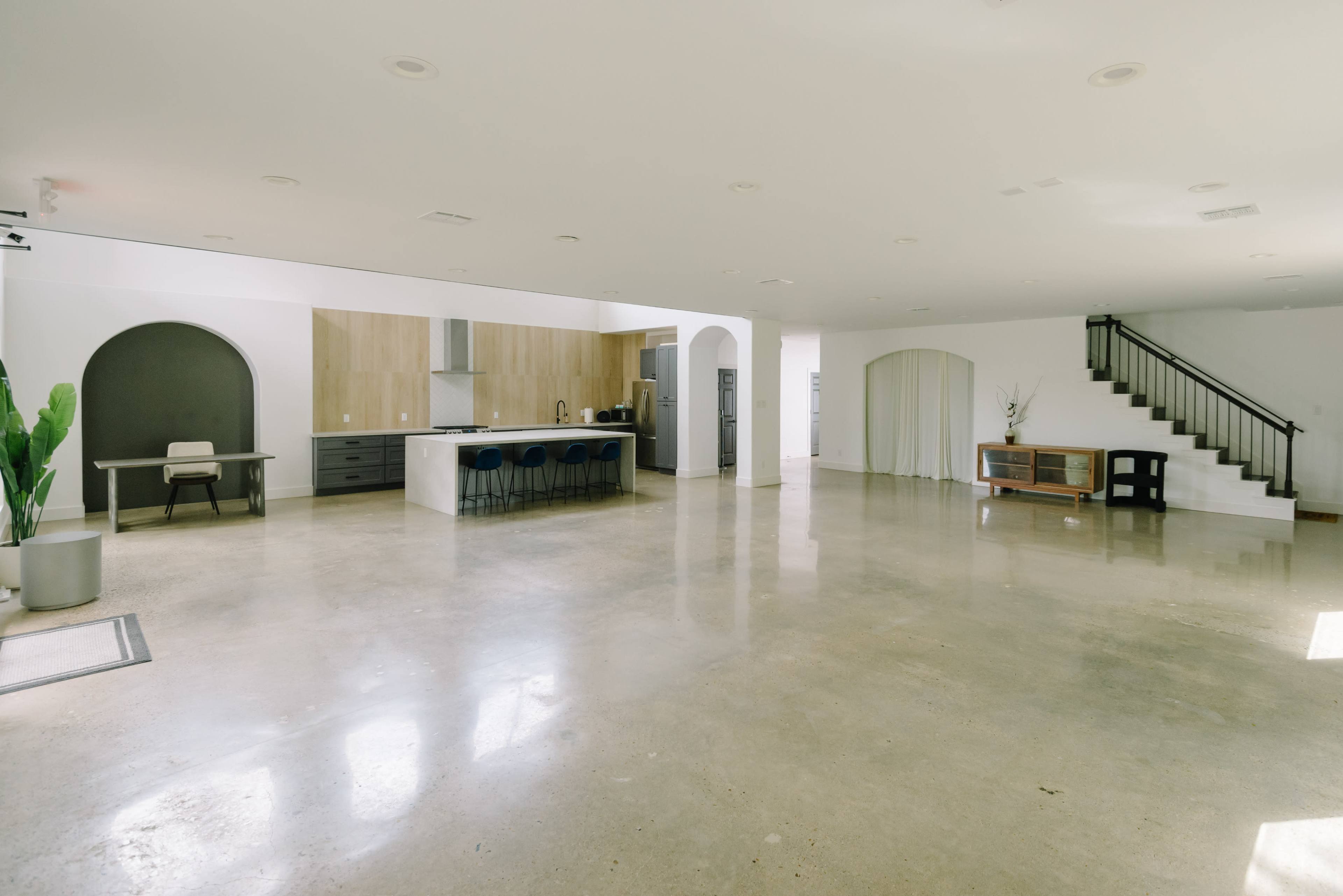 The image shows a spacious, open-concept living area with a kitchen, dining table, and a staircase in a modern interior.
