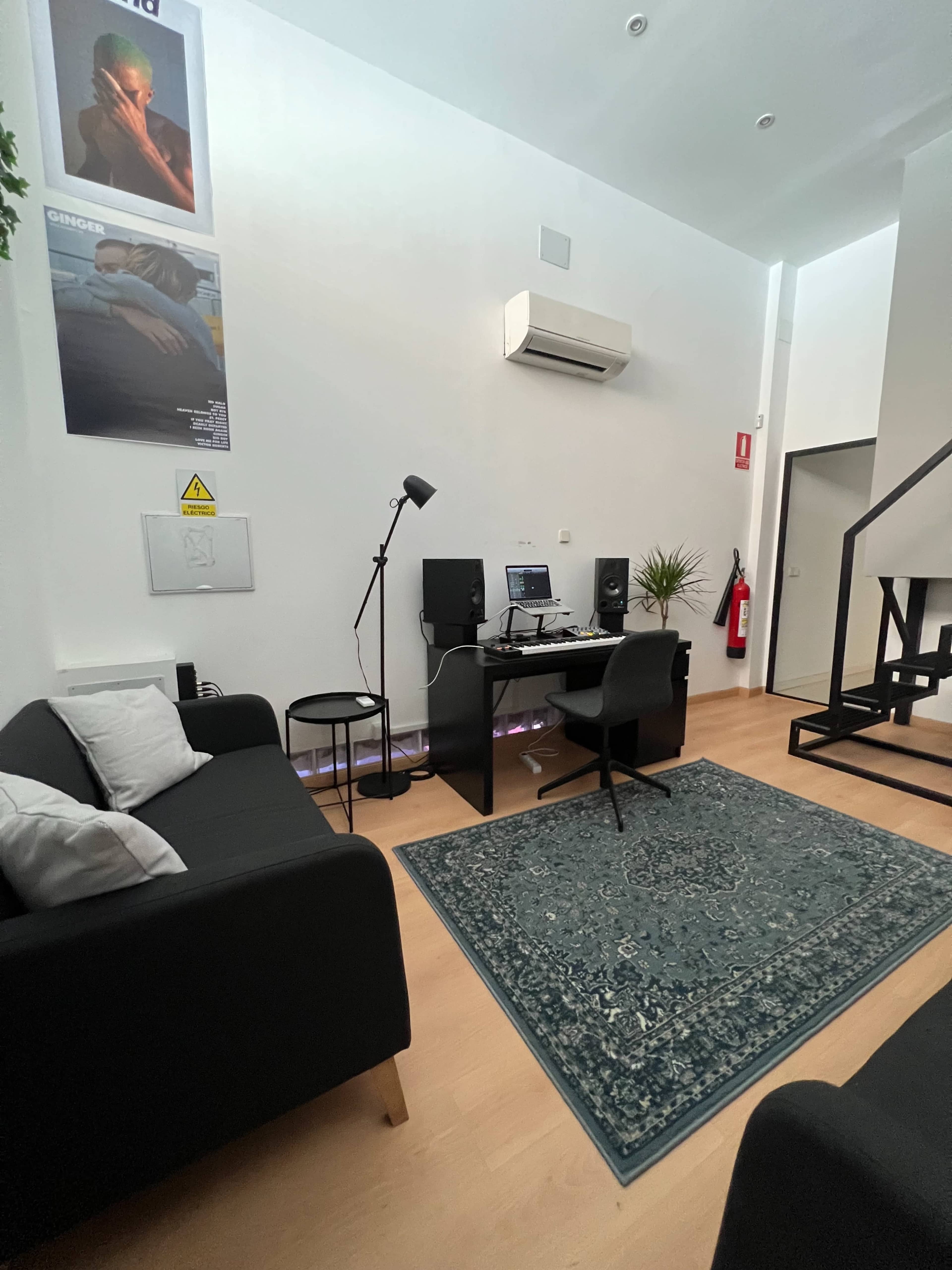 A modern office space featuring a desk with a computer setup, a black chair, a rug on the floor, and a small seating area with black couches.