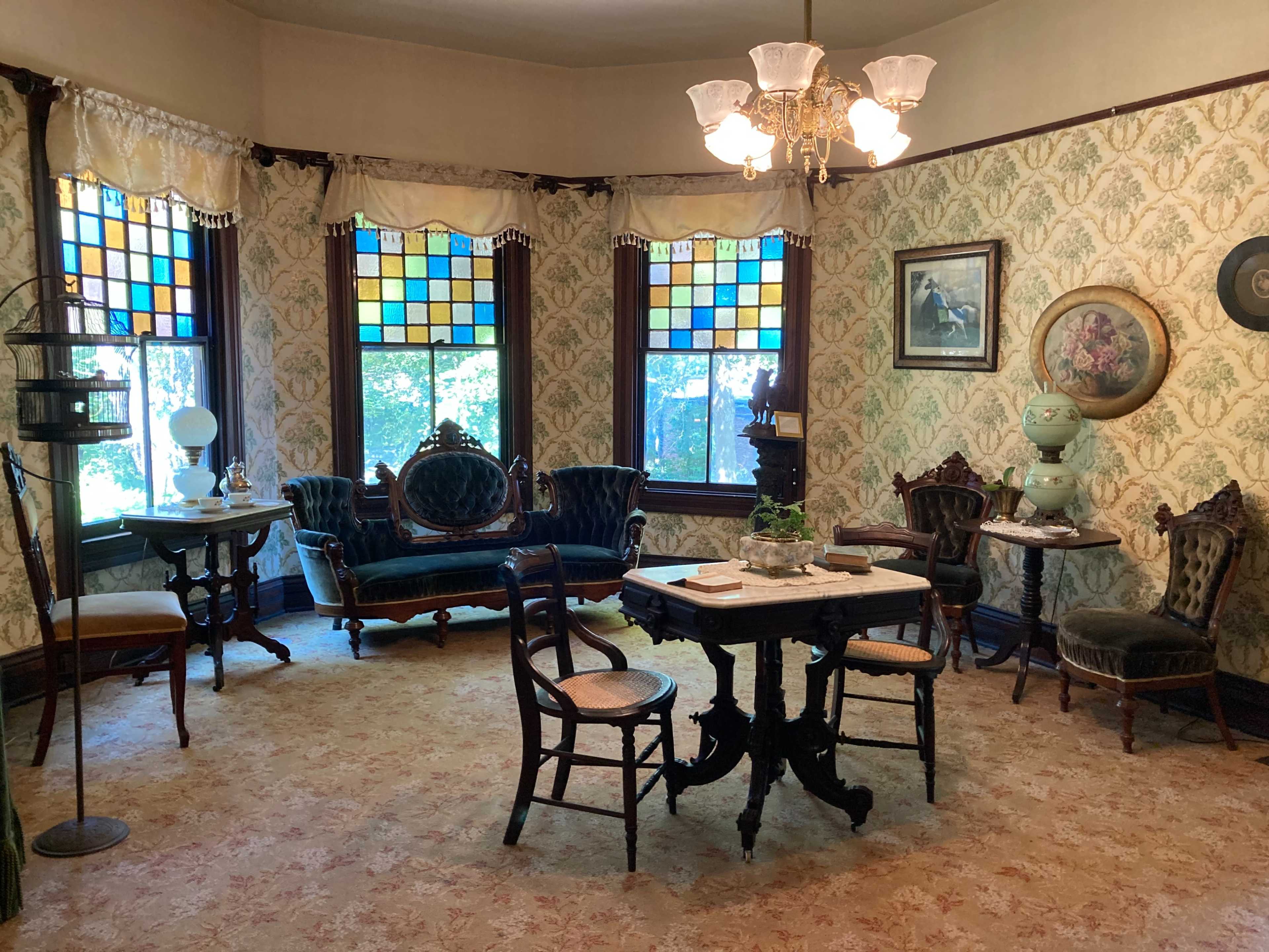 The room features vintage furniture, floral wallpaper, and stained glass windows that illuminate the space.