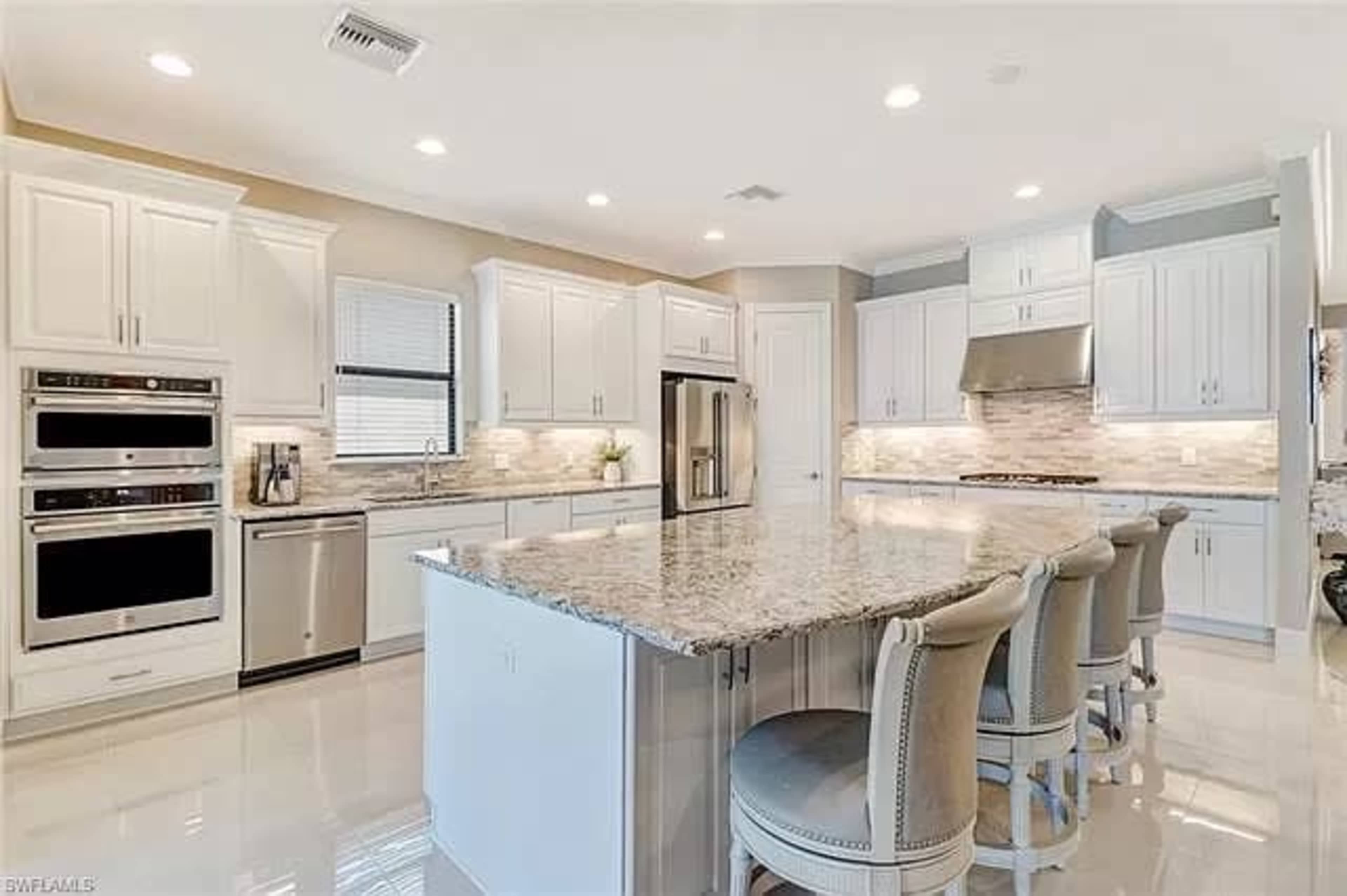 A modern kitchen with white cabinetry, granite countertops, stainless steel appliances, and an island with seating.