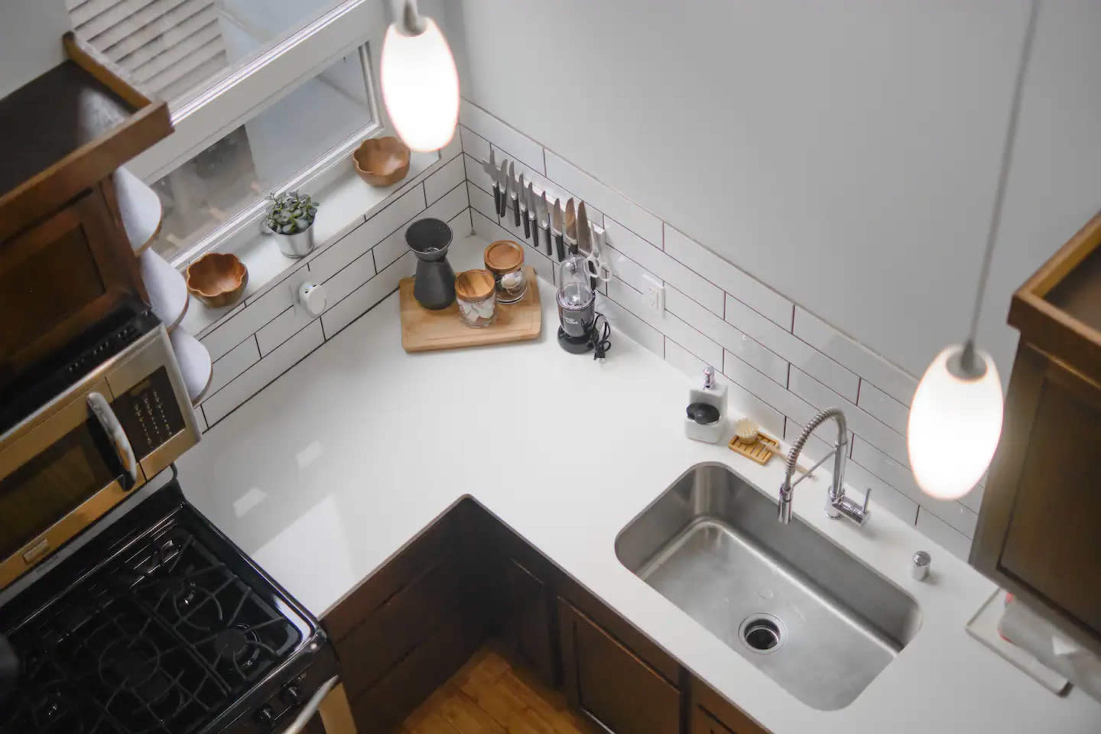 A modern kitchen with an L-shaped counter featuring a stainless steel sink, cooking utensils, and a window overhead.
