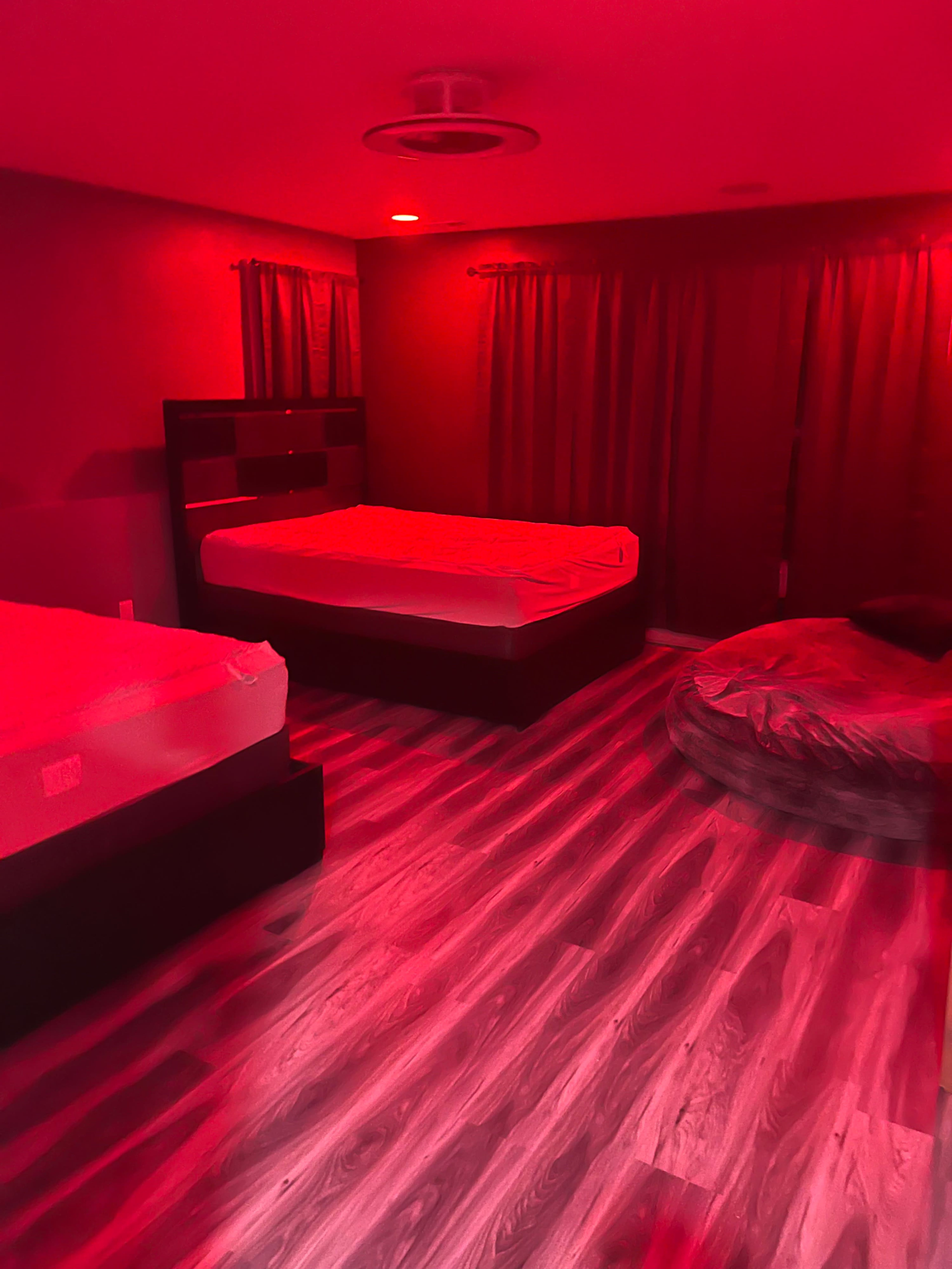The room features two unmade beds, a bean bag chair, and dim red lighting.