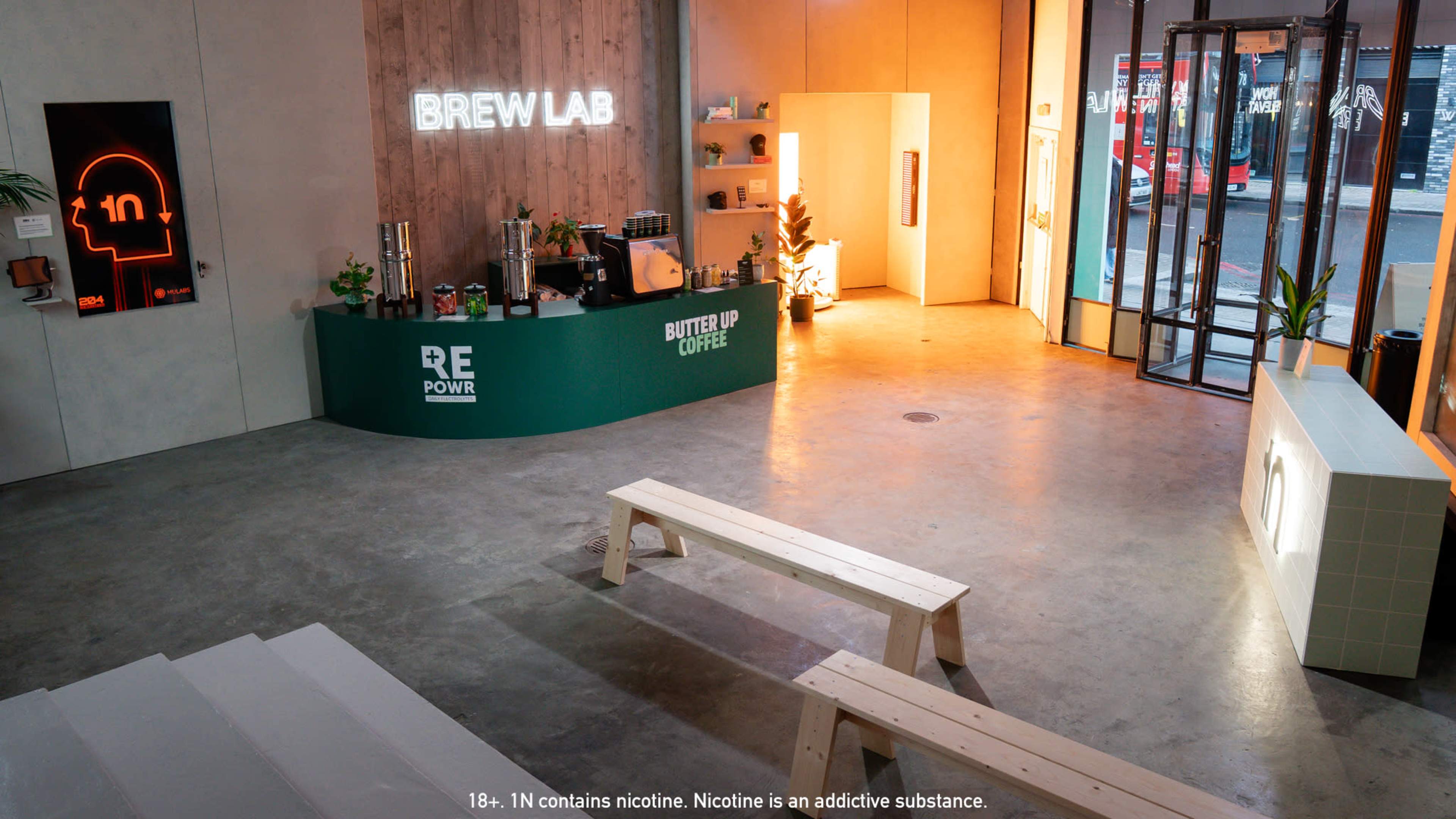 The image shows a modern café interior with a bar counter labeled "BREW LAB," wooden seating, and large windows allowing natural light to enter the space.