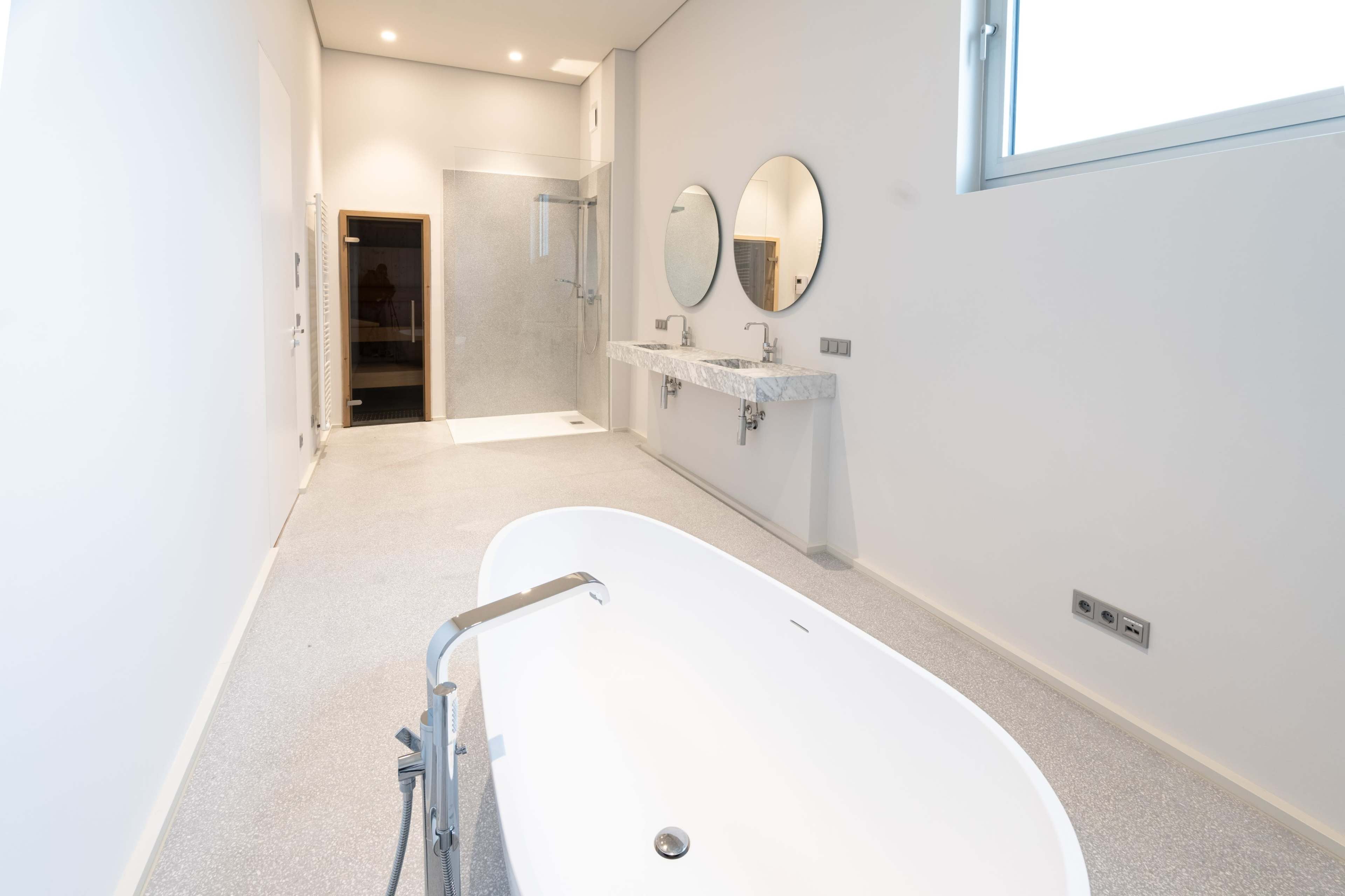 The image shows a modern bathroom featuring a freestanding bathtub, double sinks with mirrors, and a glass shower enclosure.