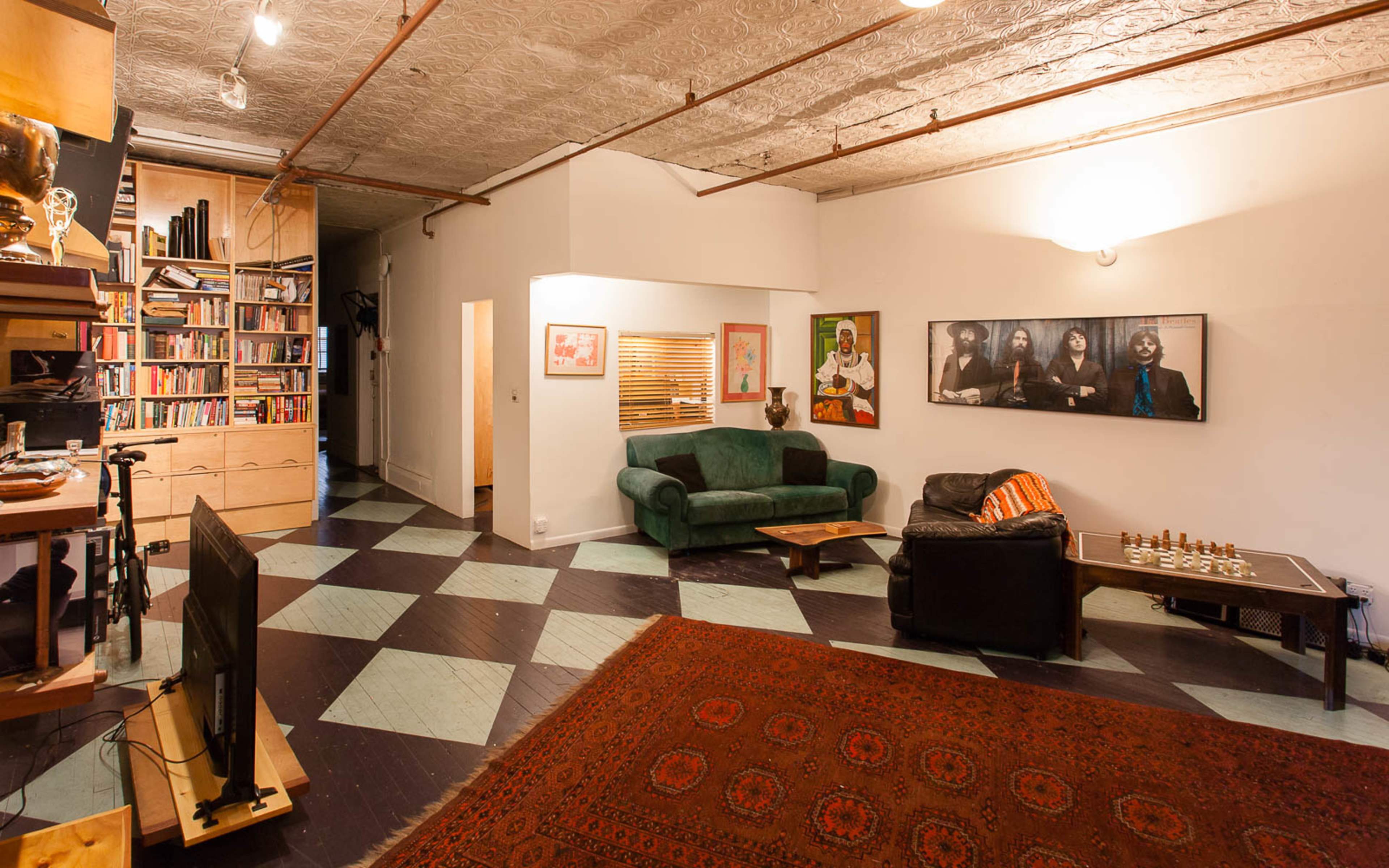A spacious living room with a green couch, a black armchair, a chess set on a table, and a patterned rug on the floor.