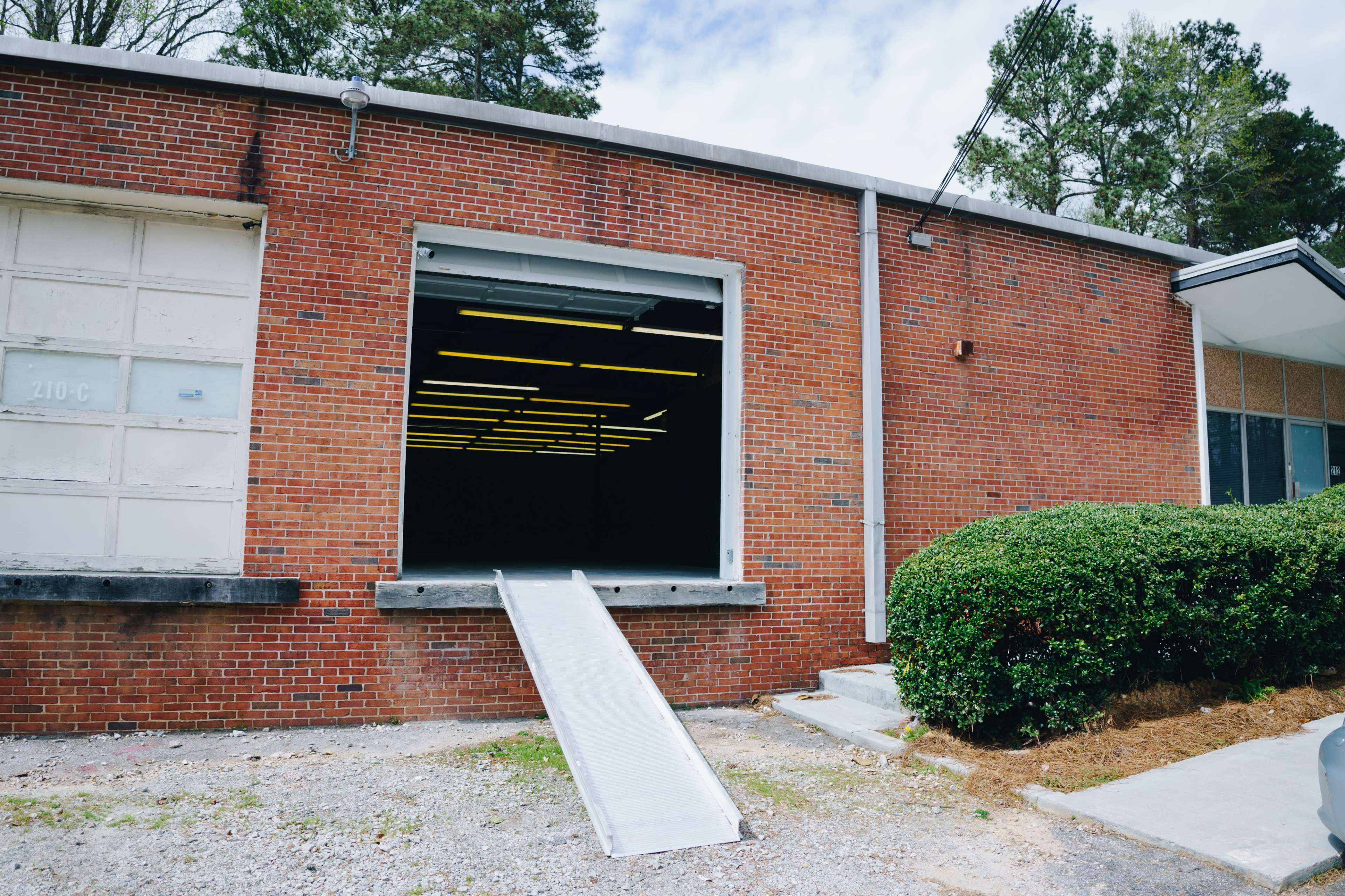 A loading dock with a ramp is attached to a brick building, featuring an open door, revealing a dark interior.