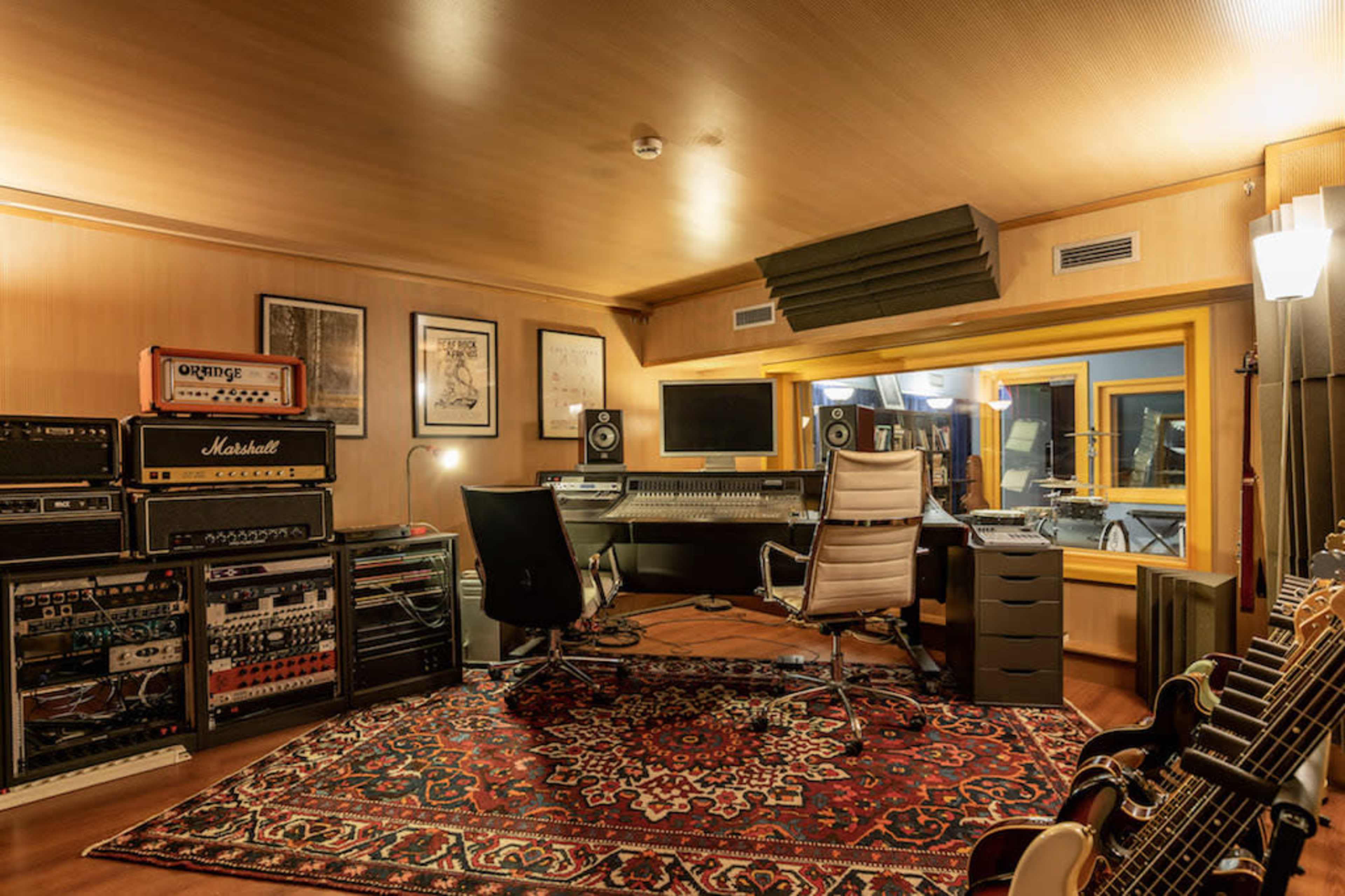 A music studio with audio equipment, a computer workstation, and guitars arranged around a patterned rug.