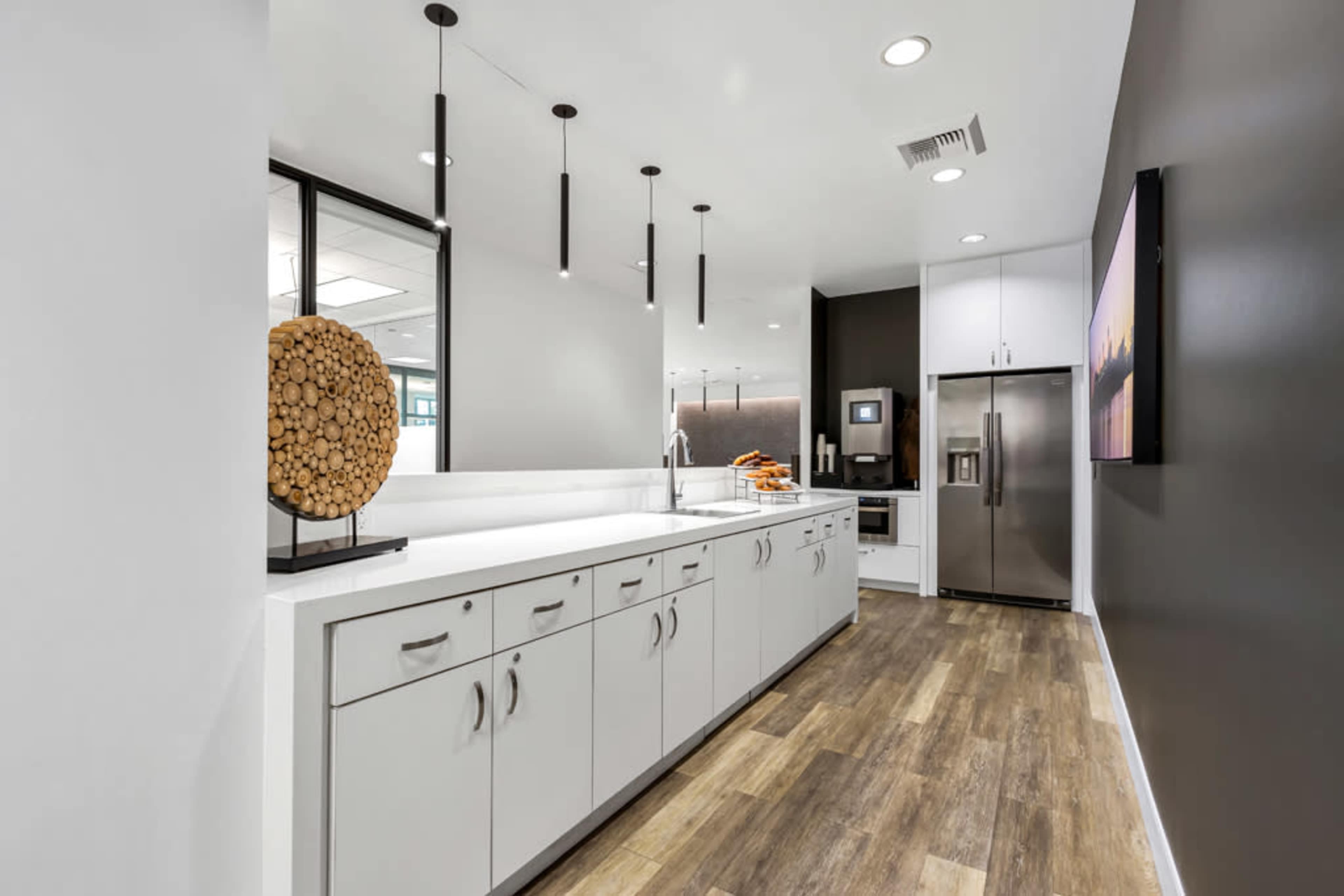 The image shows a modern kitchen with sleek cabinetry, a stainless steel refrigerator, and pendant lighting above a long countertop.