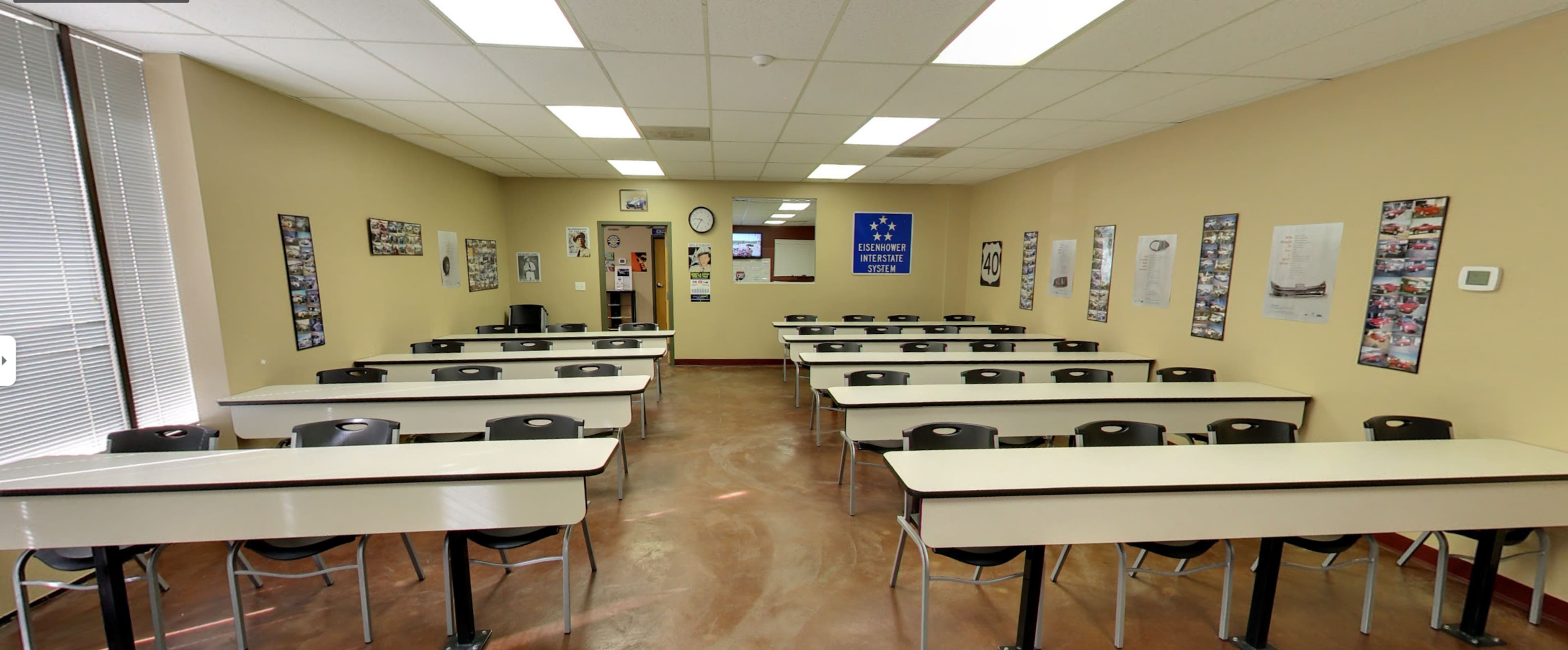 The image shows a classroom with rows of tables and chairs, posters on the walls, and a door at the back.