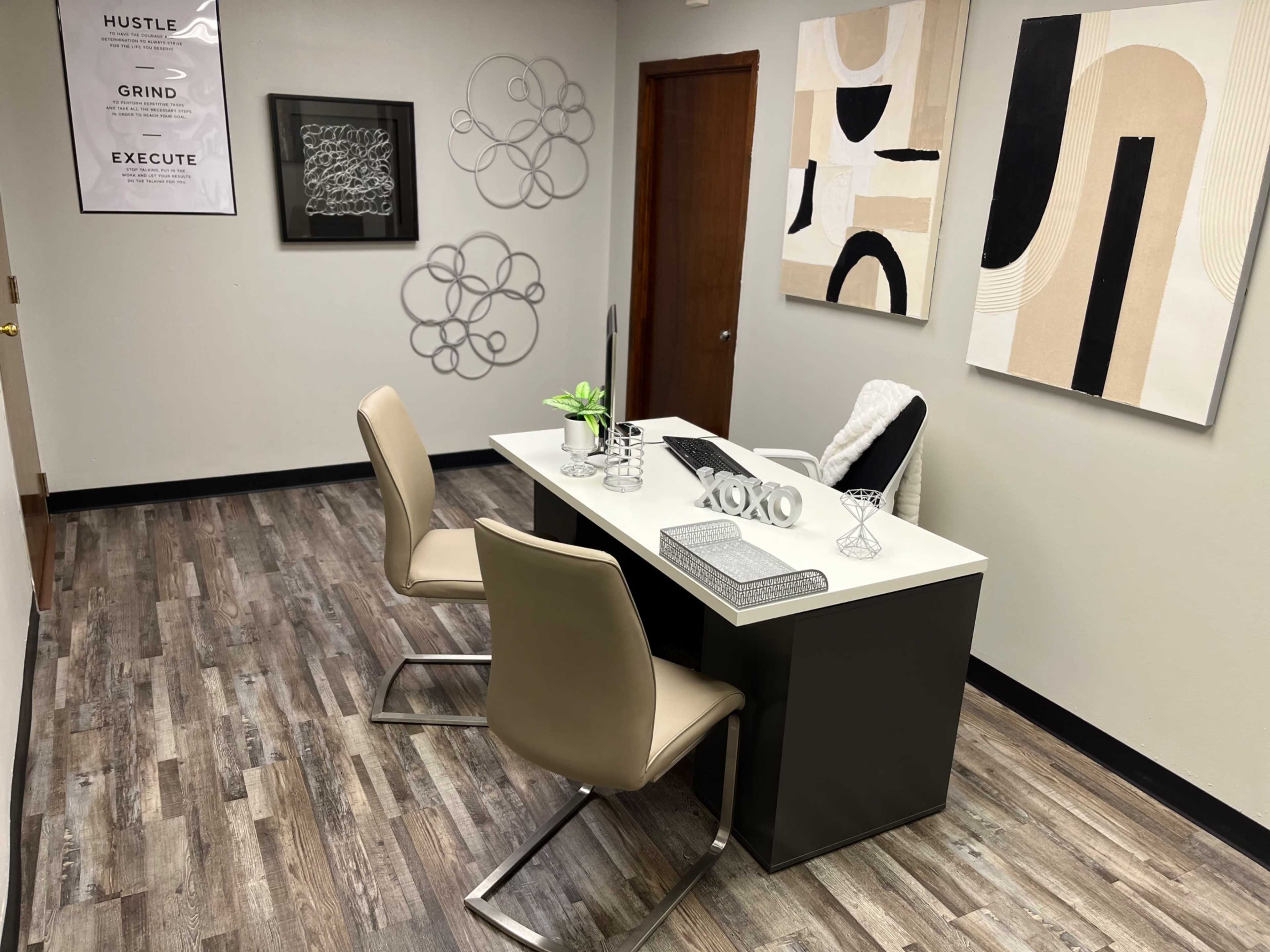 A modern office space featuring a sleek desk, two chairs, and abstract wall art.