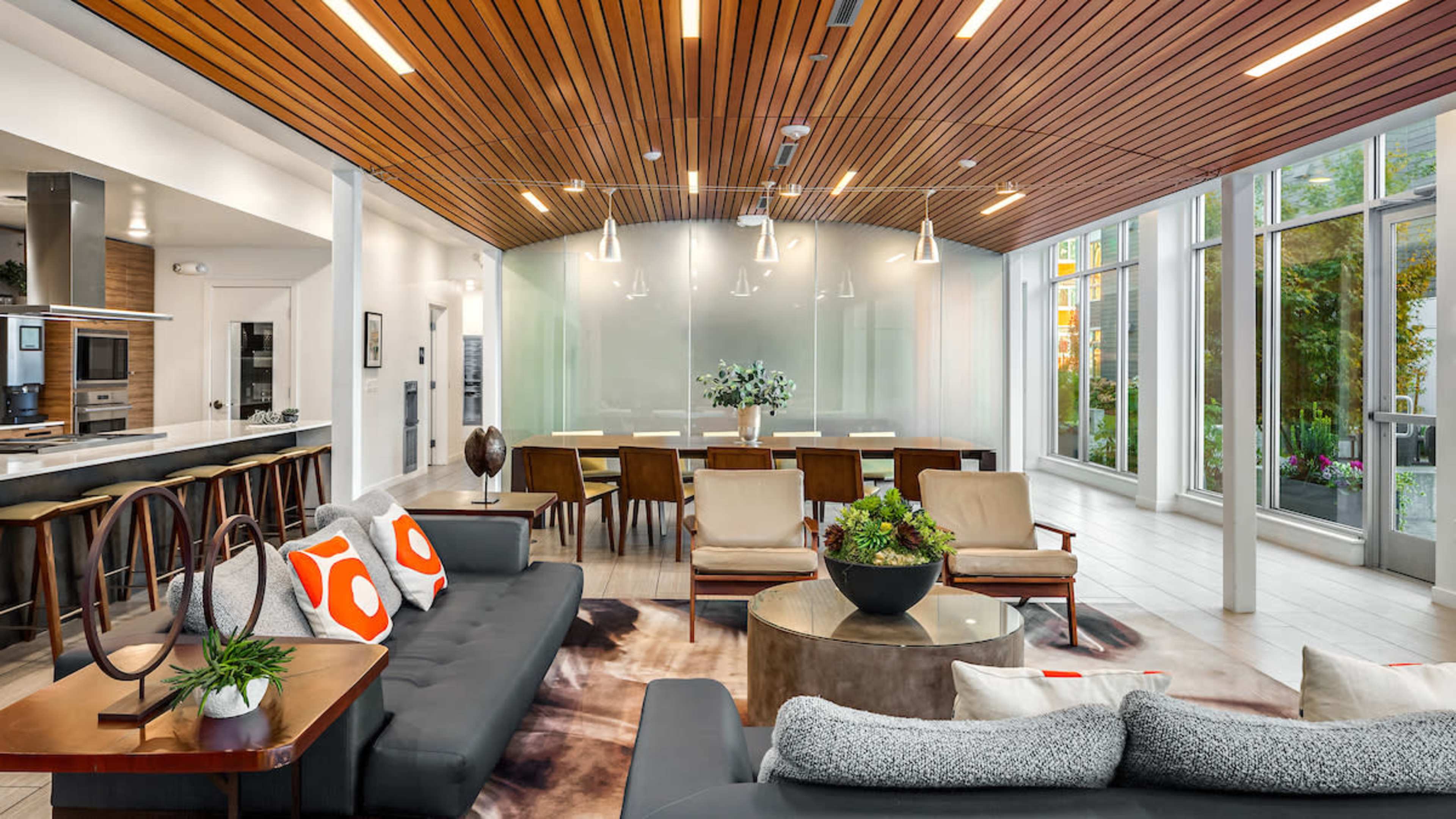 A modern open-concept living space featuring a lounge area with sofas and decorative pillows, a circular coffee table, and a dining area with a glass wall illuminated by pendant lights.