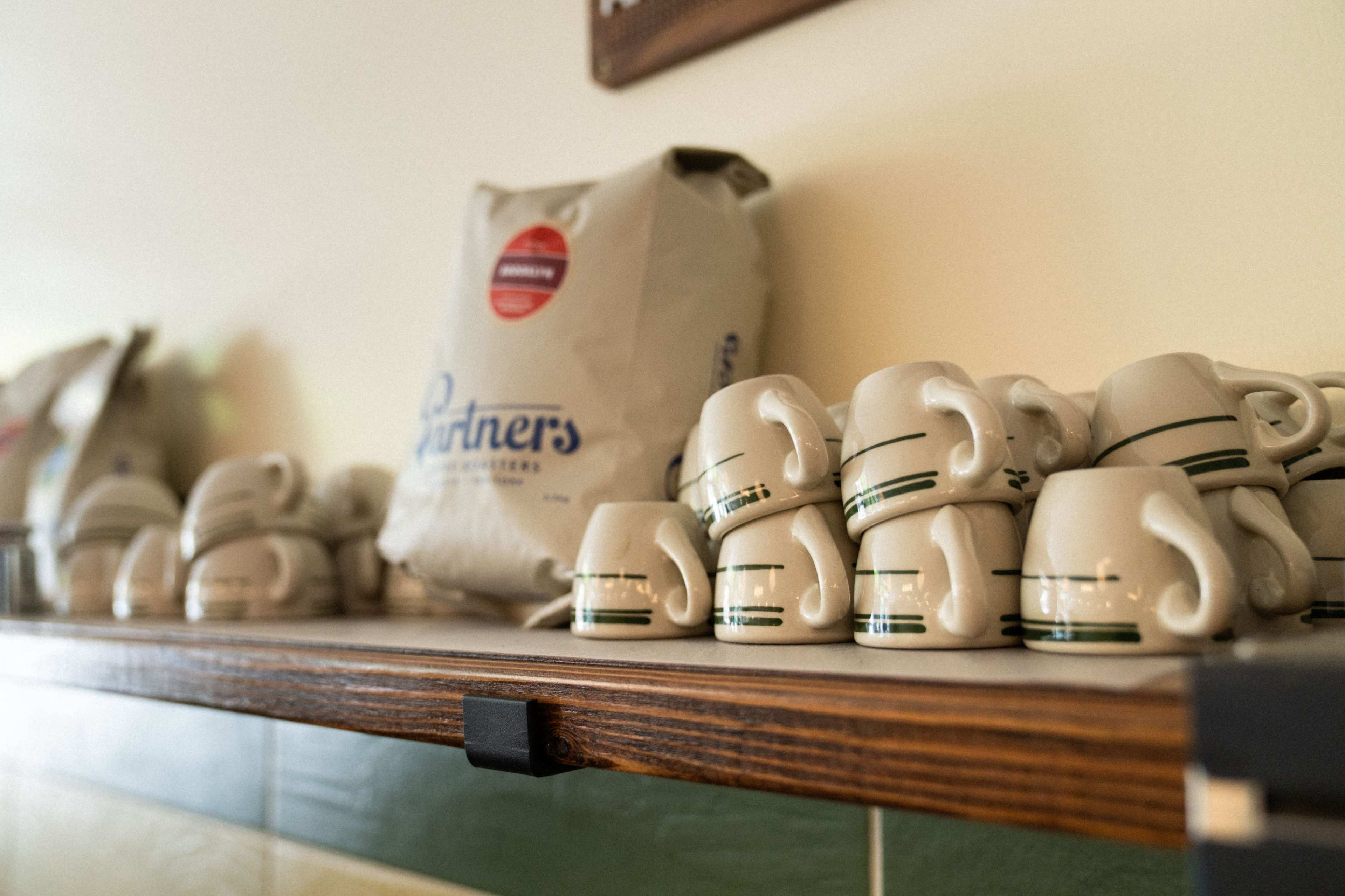 The image shows a shelf displaying stacked white coffee cups and a bag of coffee beans.