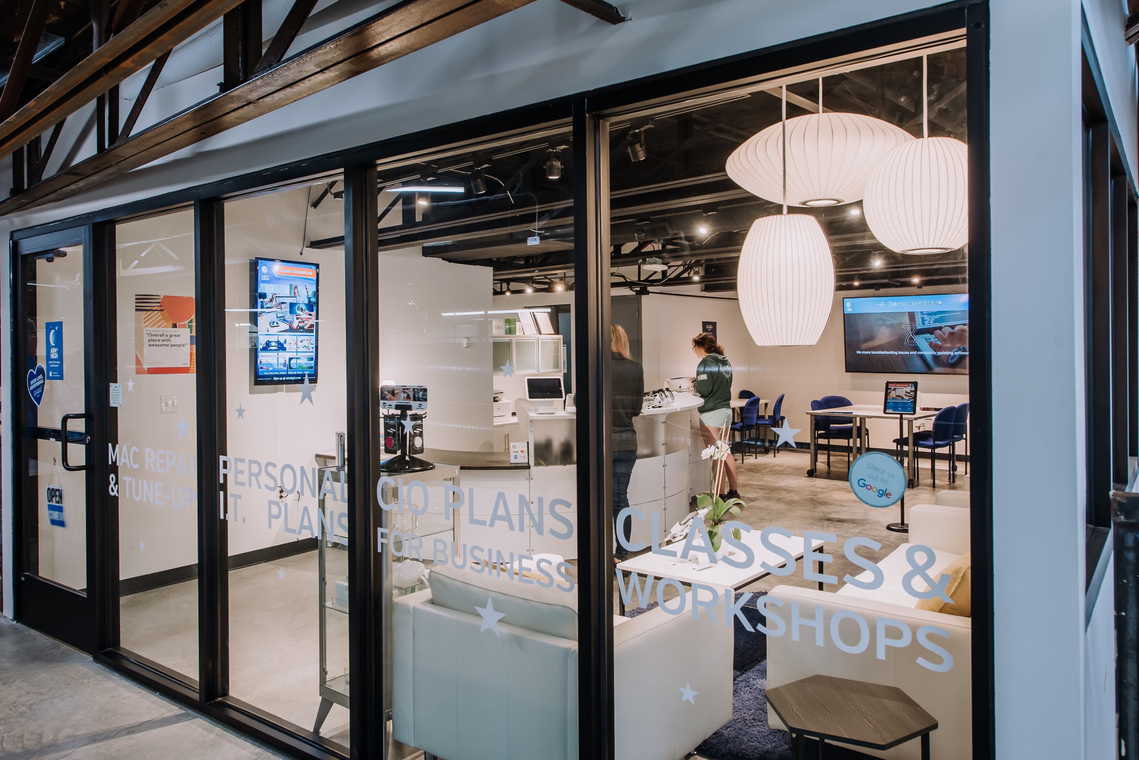 The image shows a modern office space with large windows, featuring seating areas and informational displays about classes and business plans.