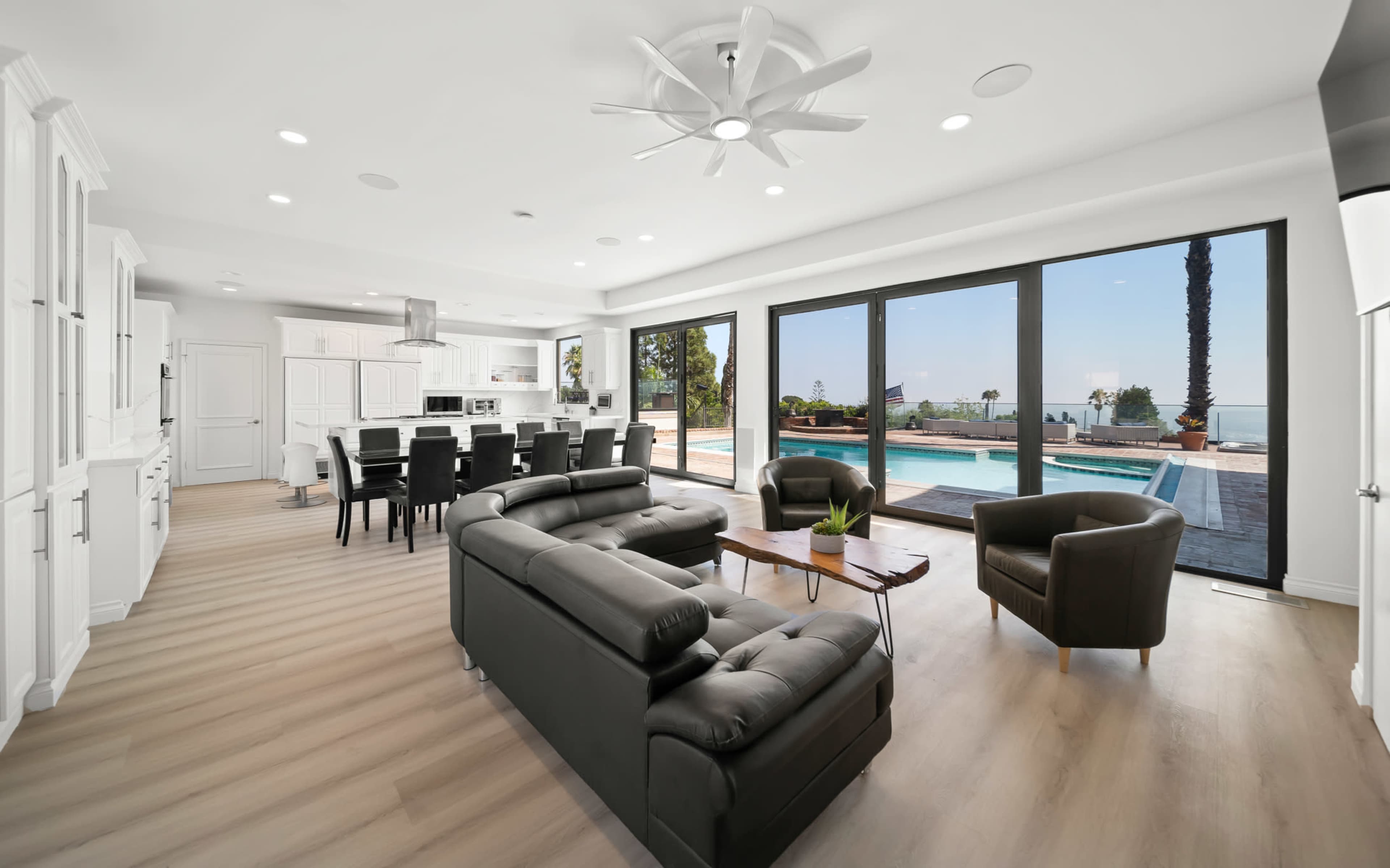 A modern living space with a black sofa, a dining area, and large glass doors opening to a poolside view.