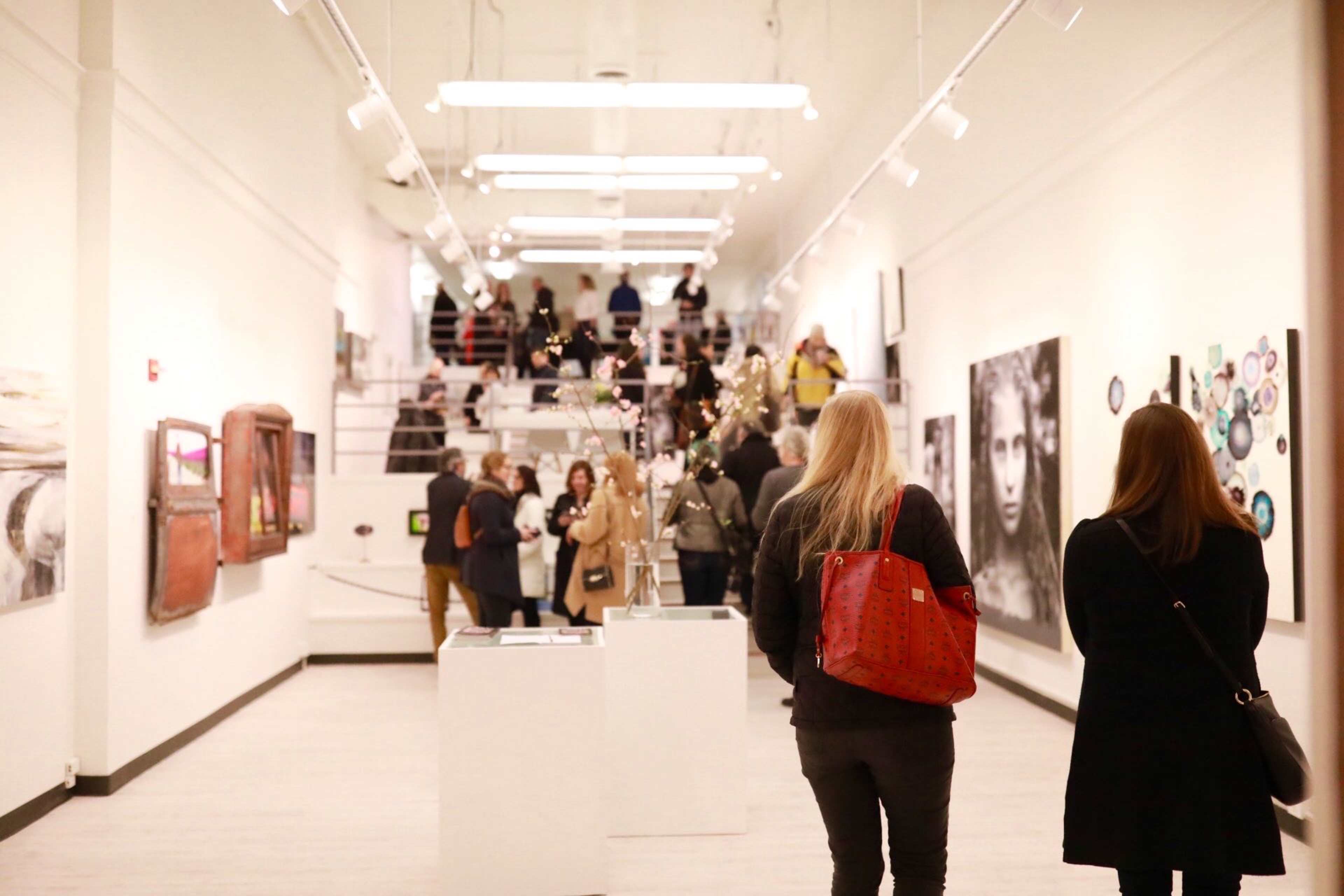A crowded art gallery with people examining various artworks displayed on the walls.