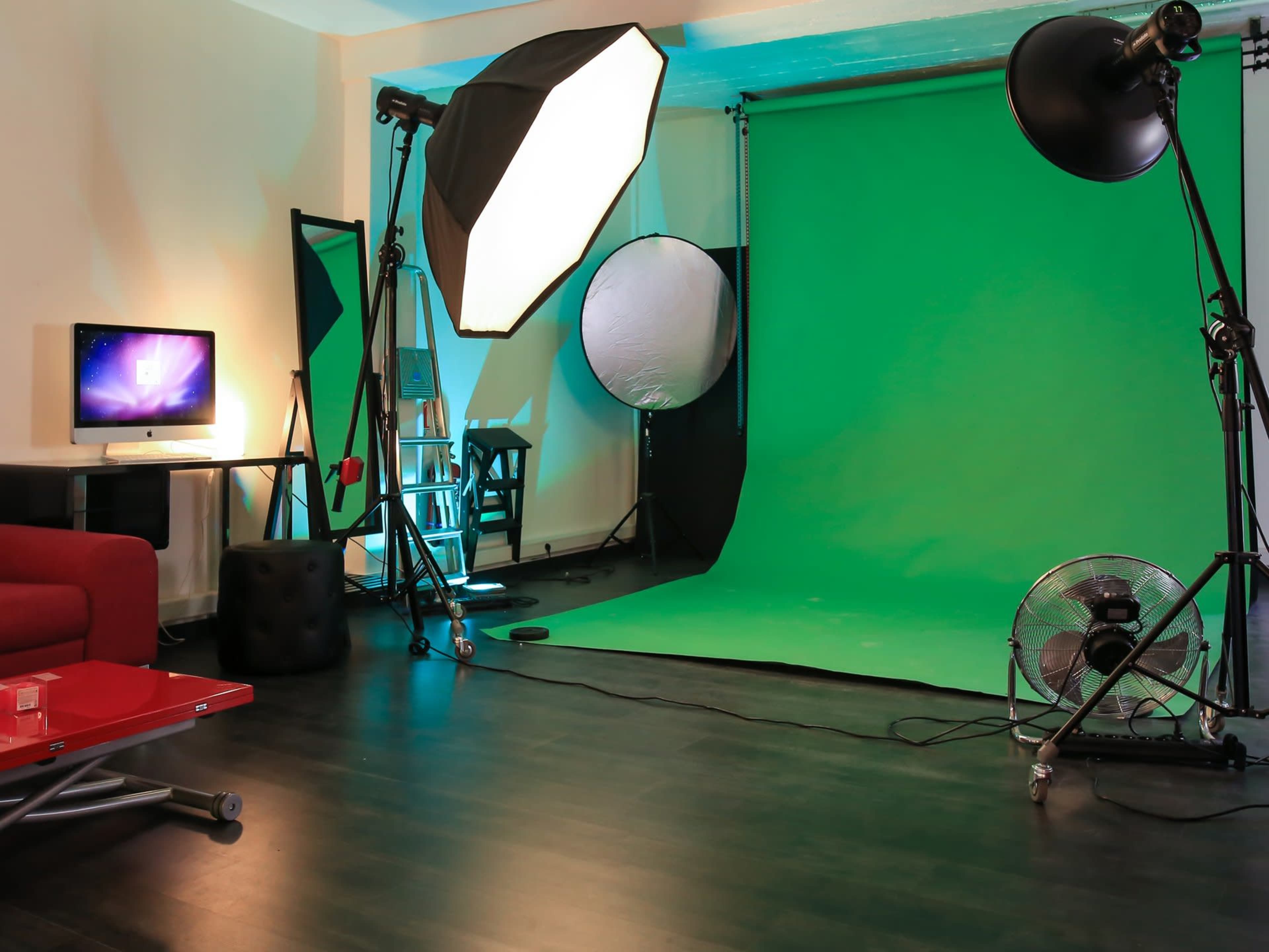 The image shows a photo studio setup with a green backdrop, lighting equipment, and a computer on a table.