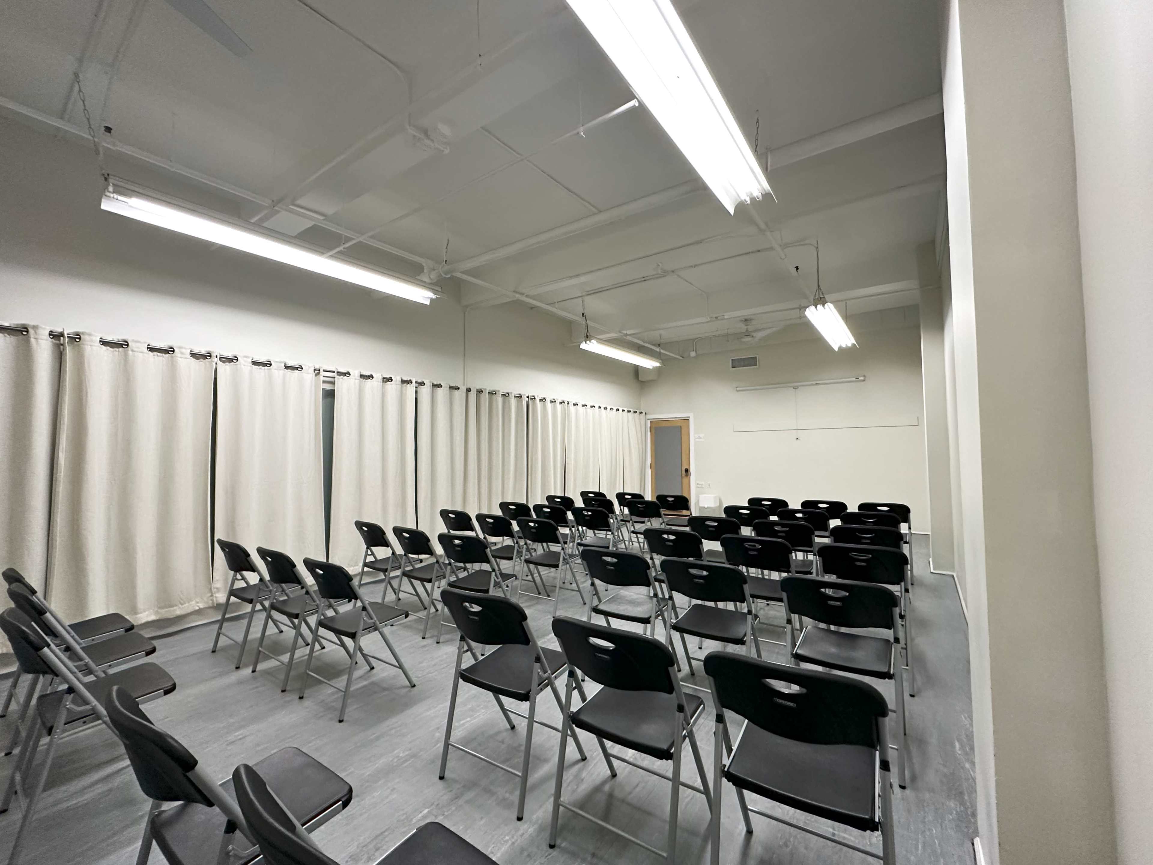 A room with several rows of black folding chairs arranged neatly, illuminated by overhead fluorescent lights.