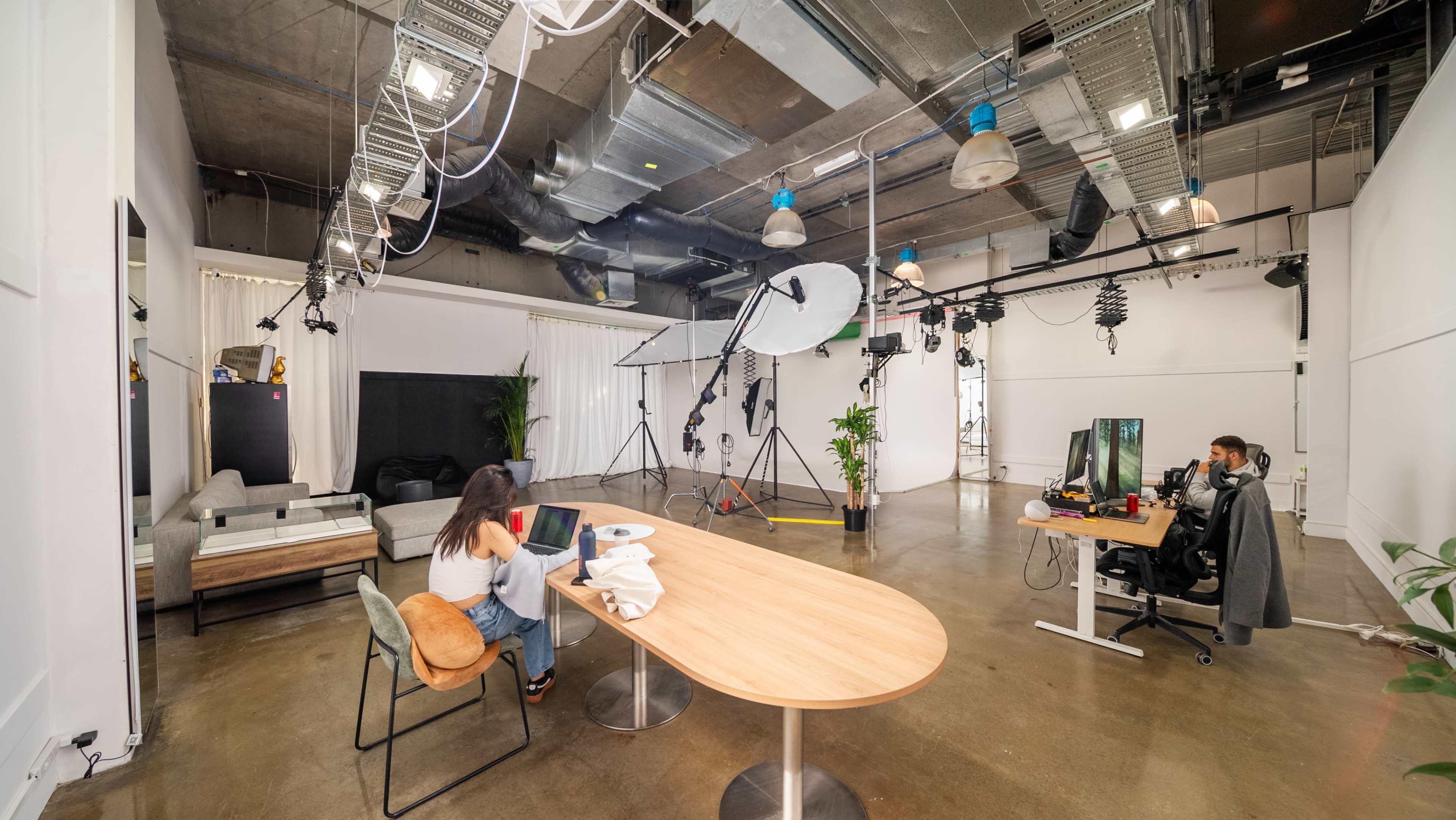 The image shows a spacious studio with a large round light setup, two workstations, a table, and seating areas.