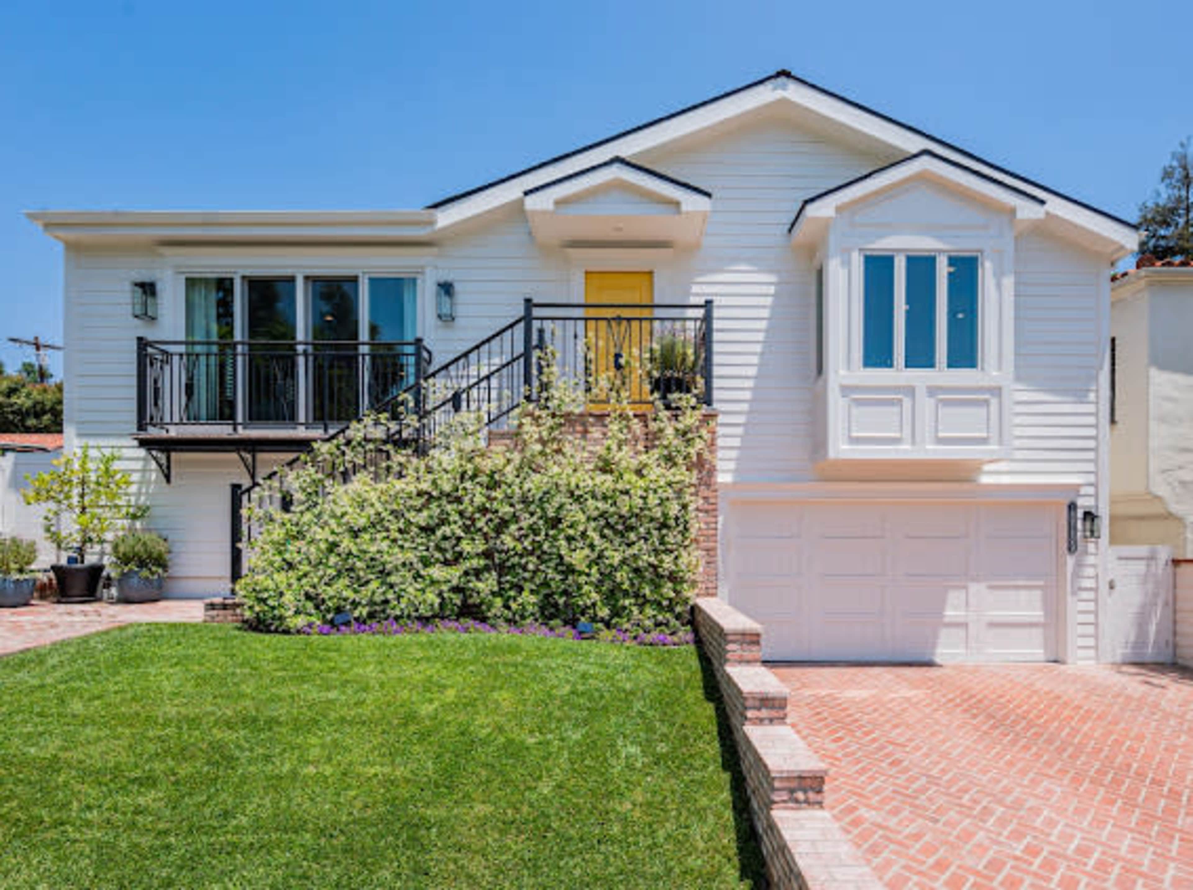 A two-story house with a bright yellow front door, surrounded by well-maintained landscaping and brick pathways.