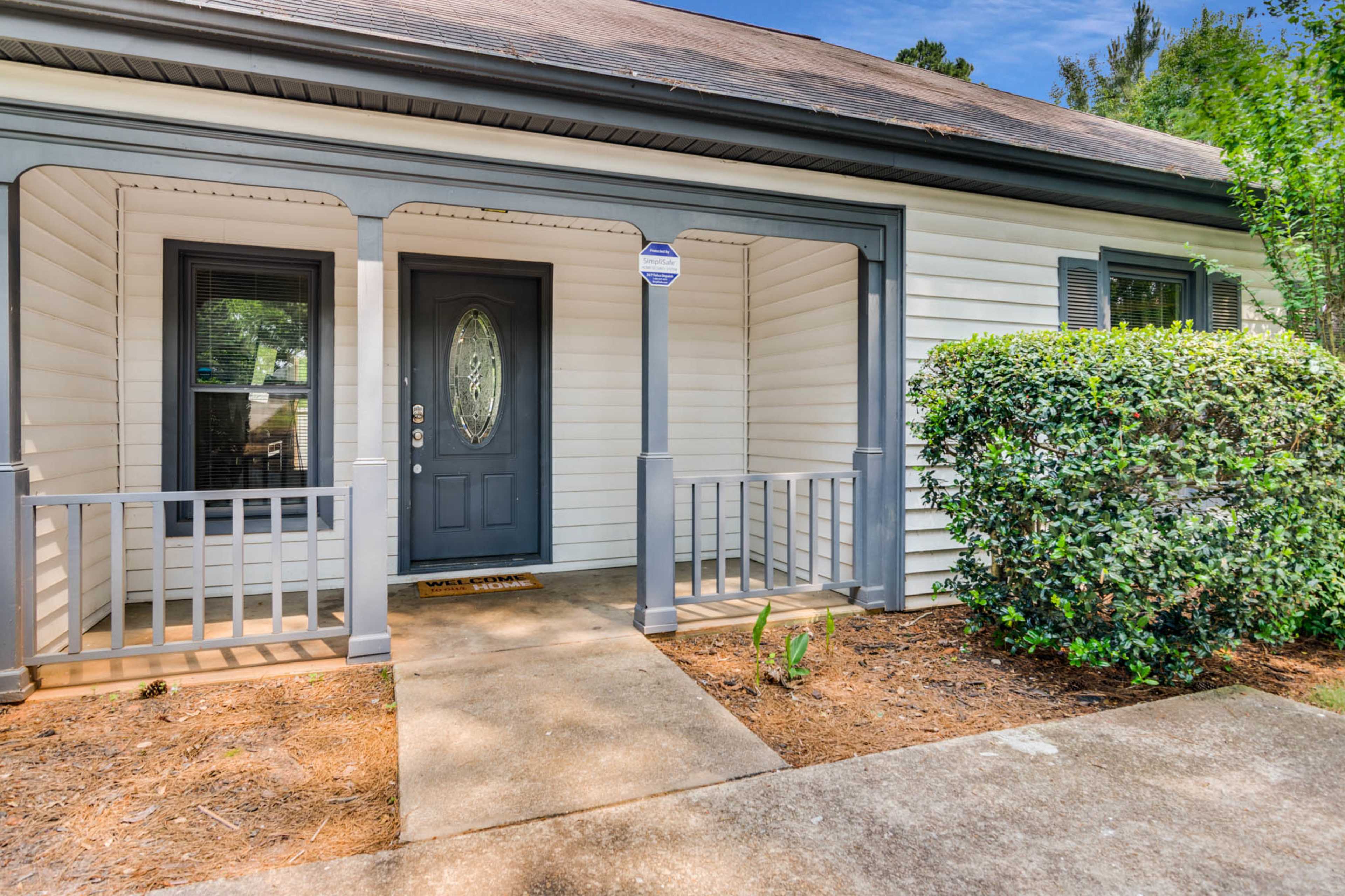 The image shows the entrance of a house with a front porch, a dark-colored door, and neatly trimmed shrubs on either side.