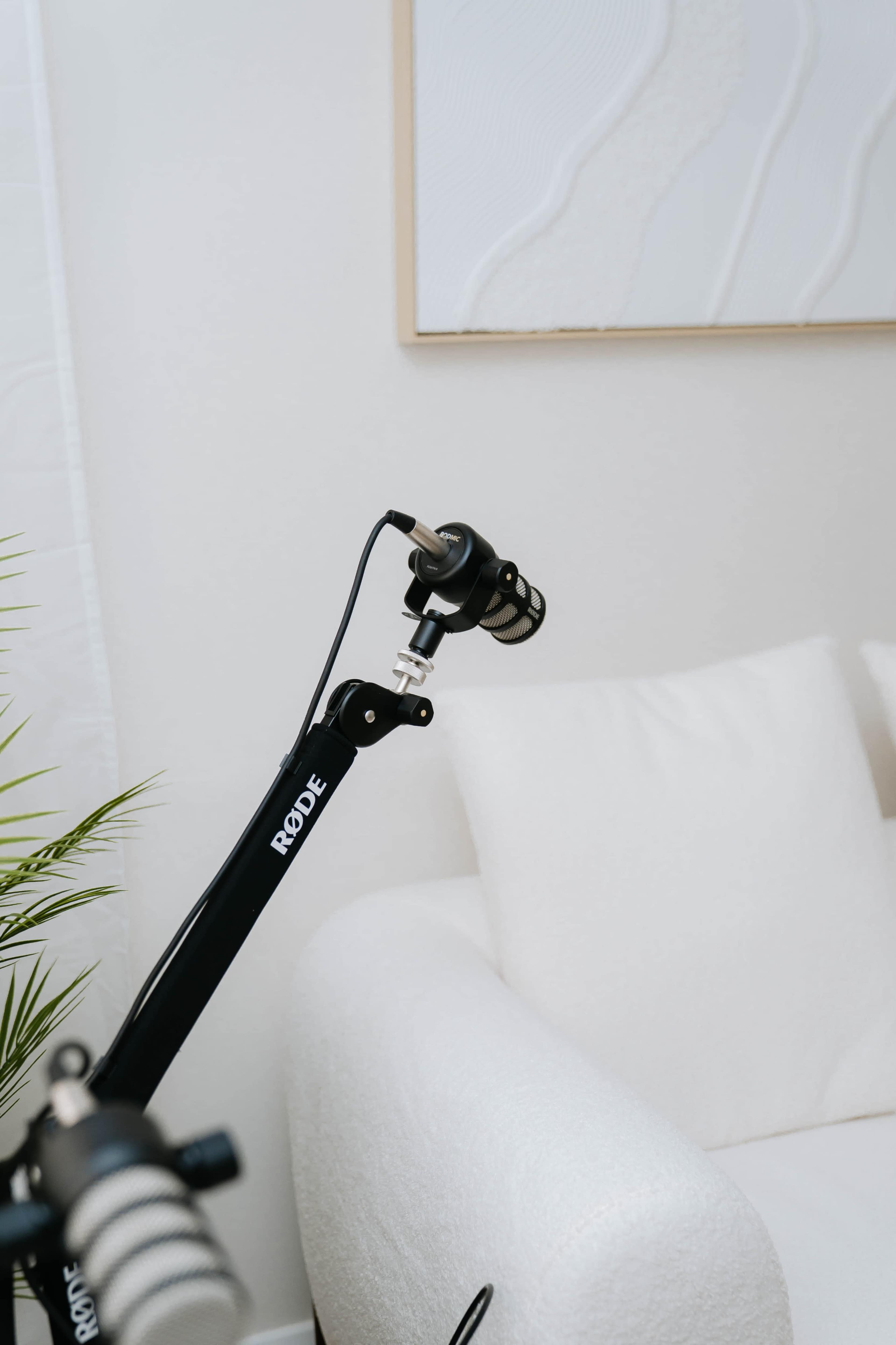 A black microphone is mounted on an adjustable arm next to a white couch in a light-colored room.