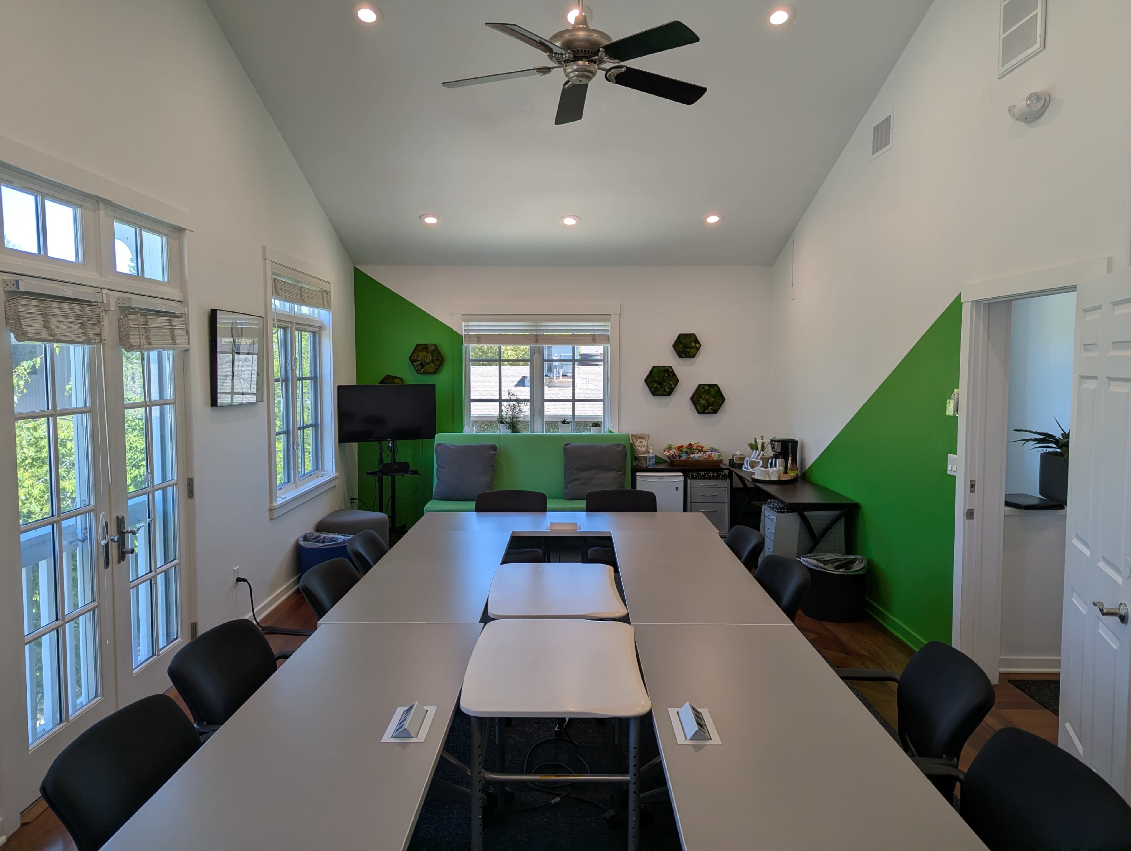 A modern conference room features a long gray table surrounded by black chairs, green accent walls, and a wall-mounted screen.