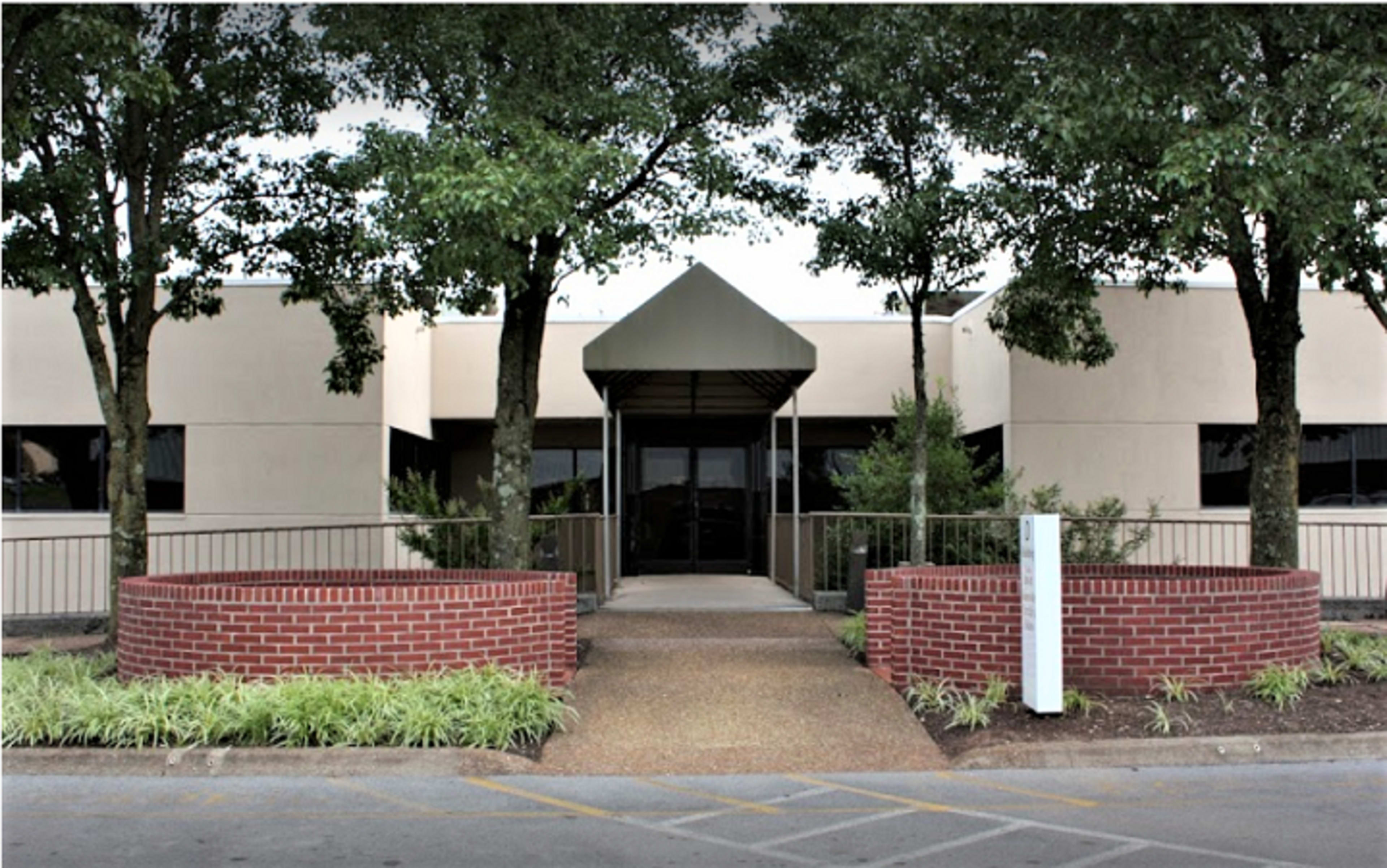 The entrance of a modern building flanked by two trees and surrounded by brick planters.
