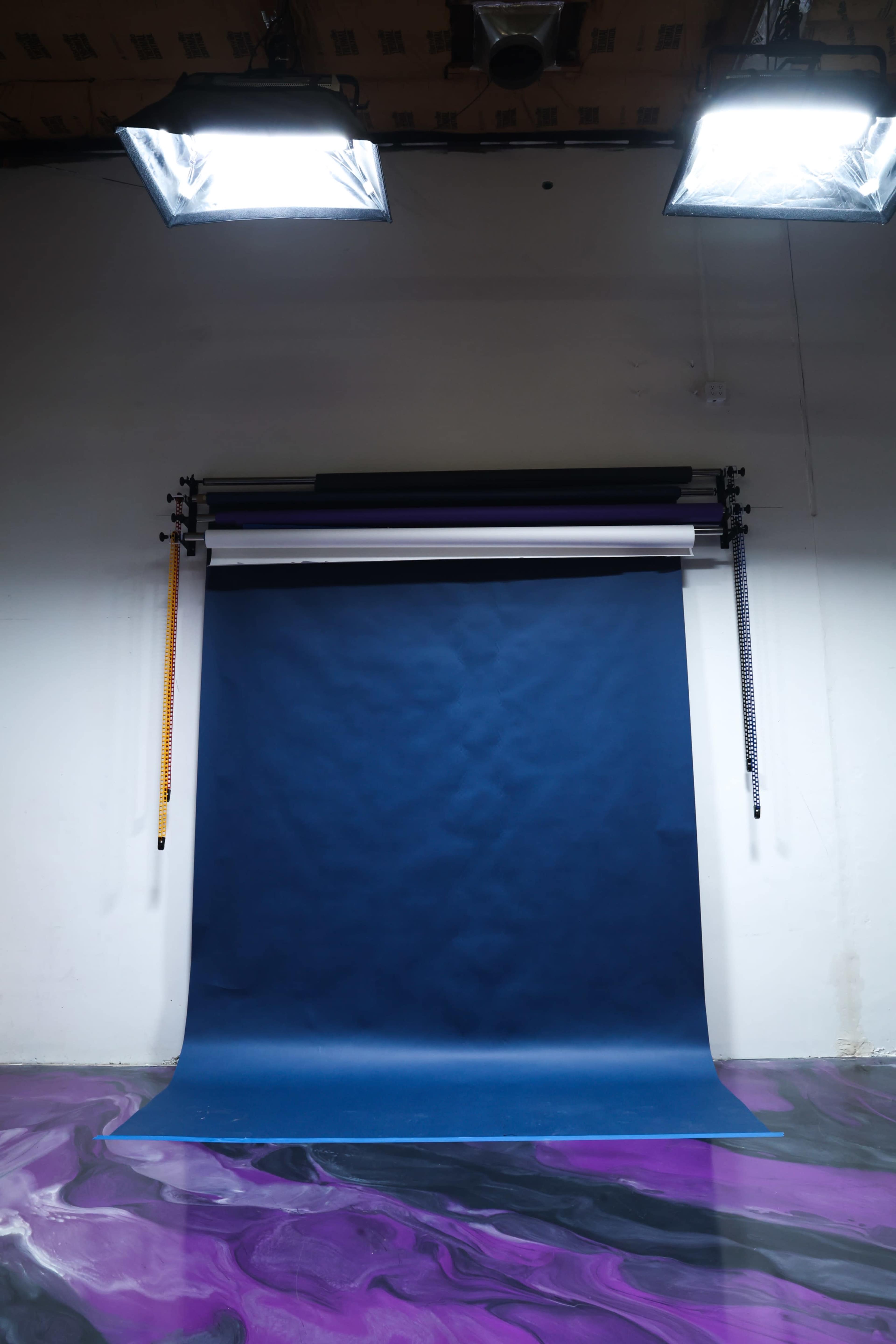 A photography studio is set up with a blue backdrop and softbox lights above it, placed on a marbled purple floor.